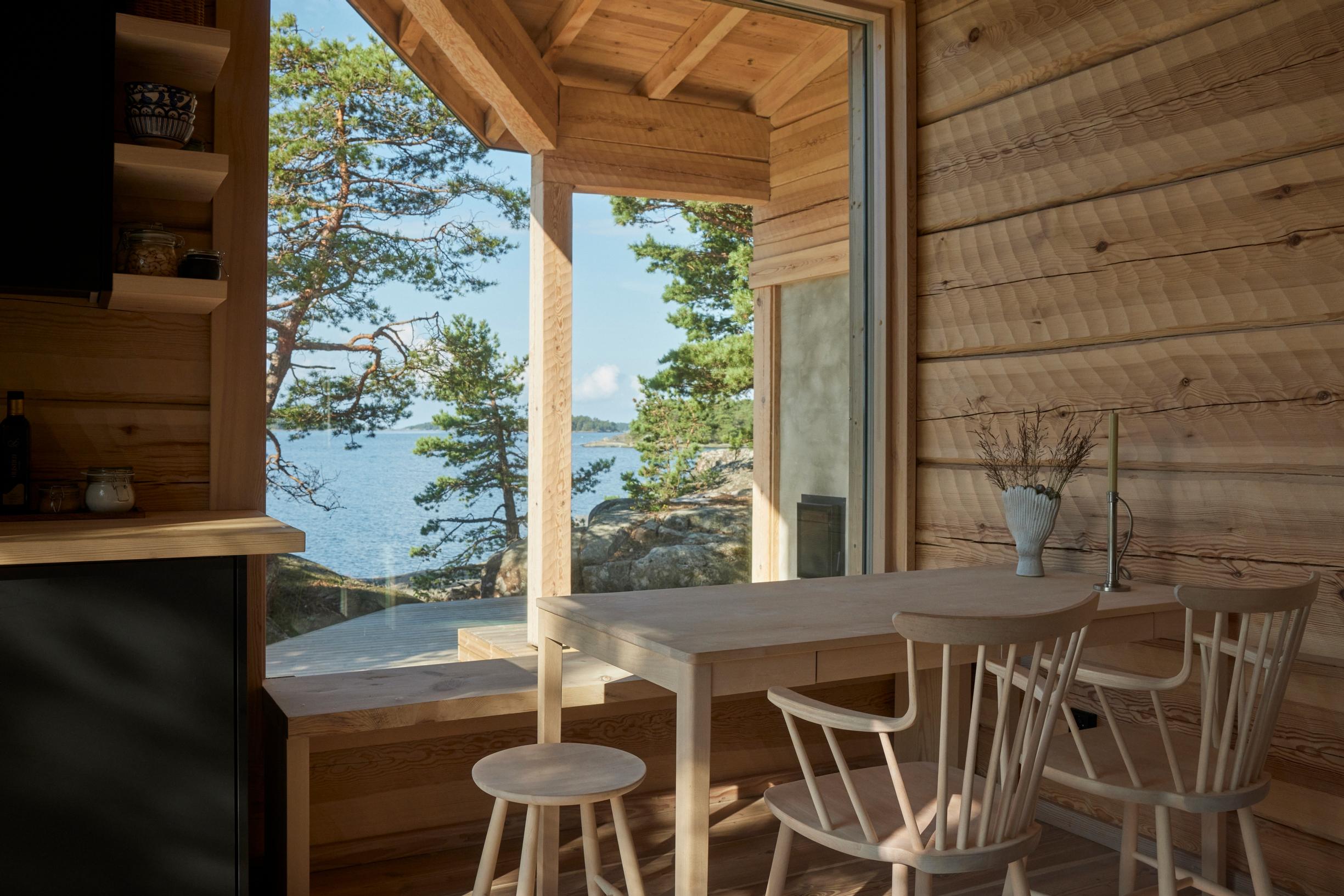 A few wooden chairs and a table by the window in the sauna living area.