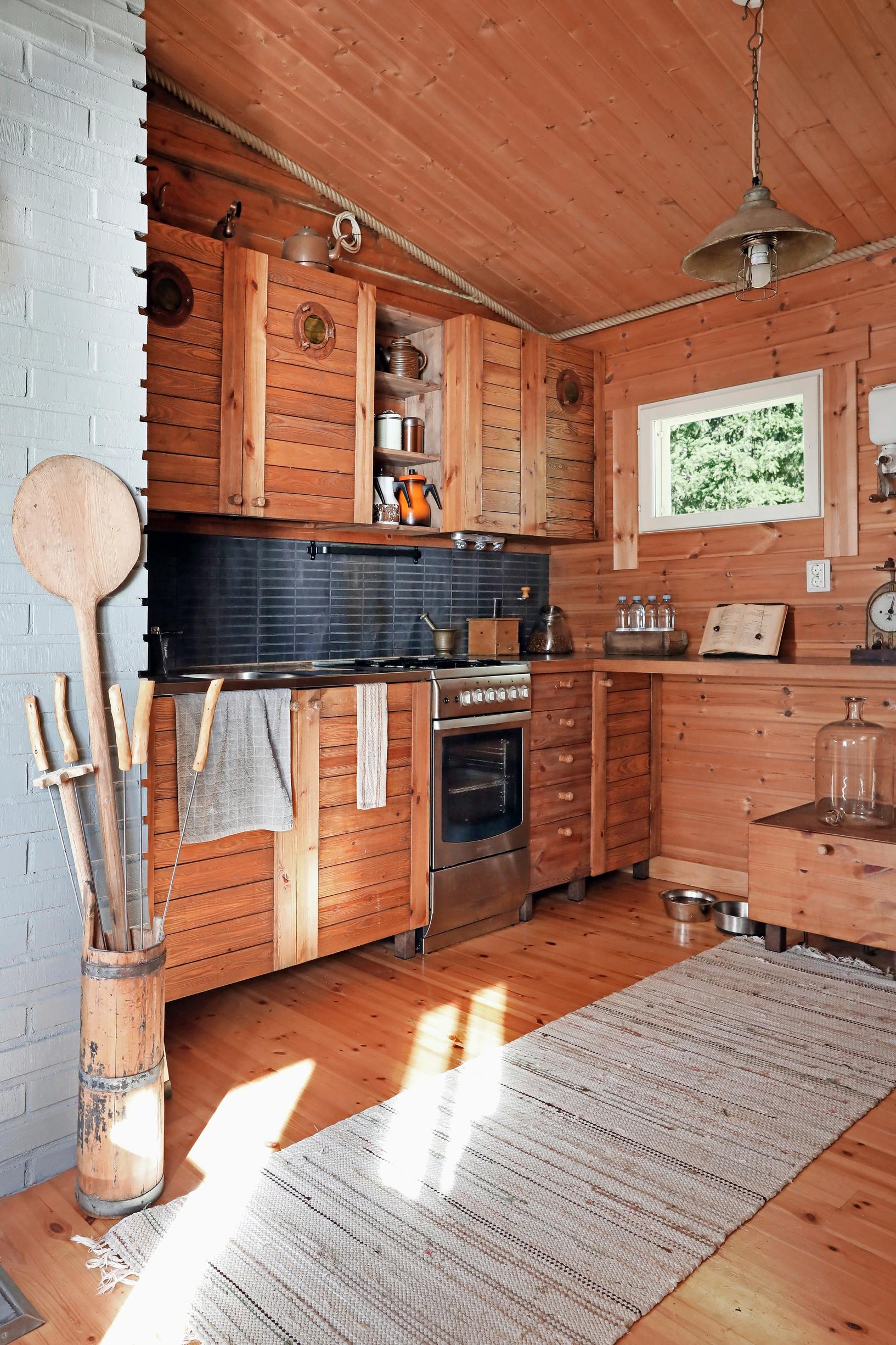 Wooden kitchen cabinets, a rag rug, wood walls and floor, and an old pail.