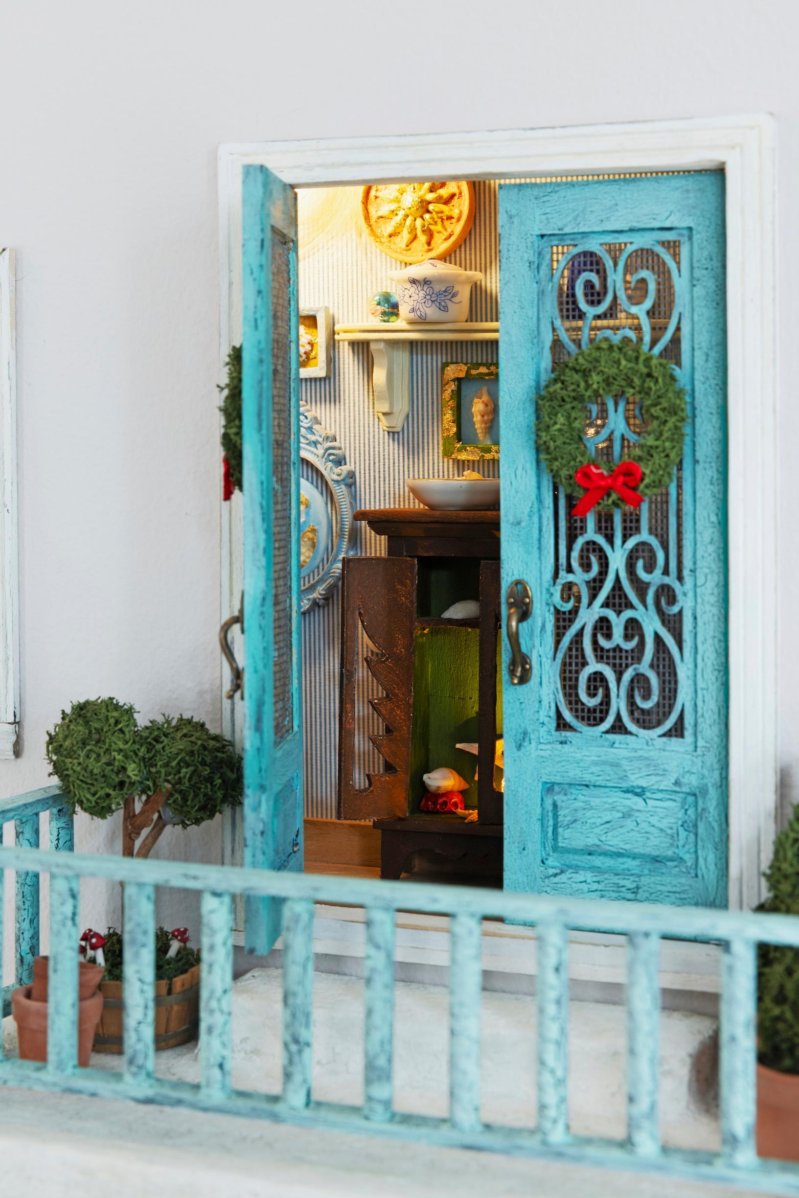 A Mamma Mia–themed elf door balcony with a turquoise door and rail, evoking a Mediterranean vibe.