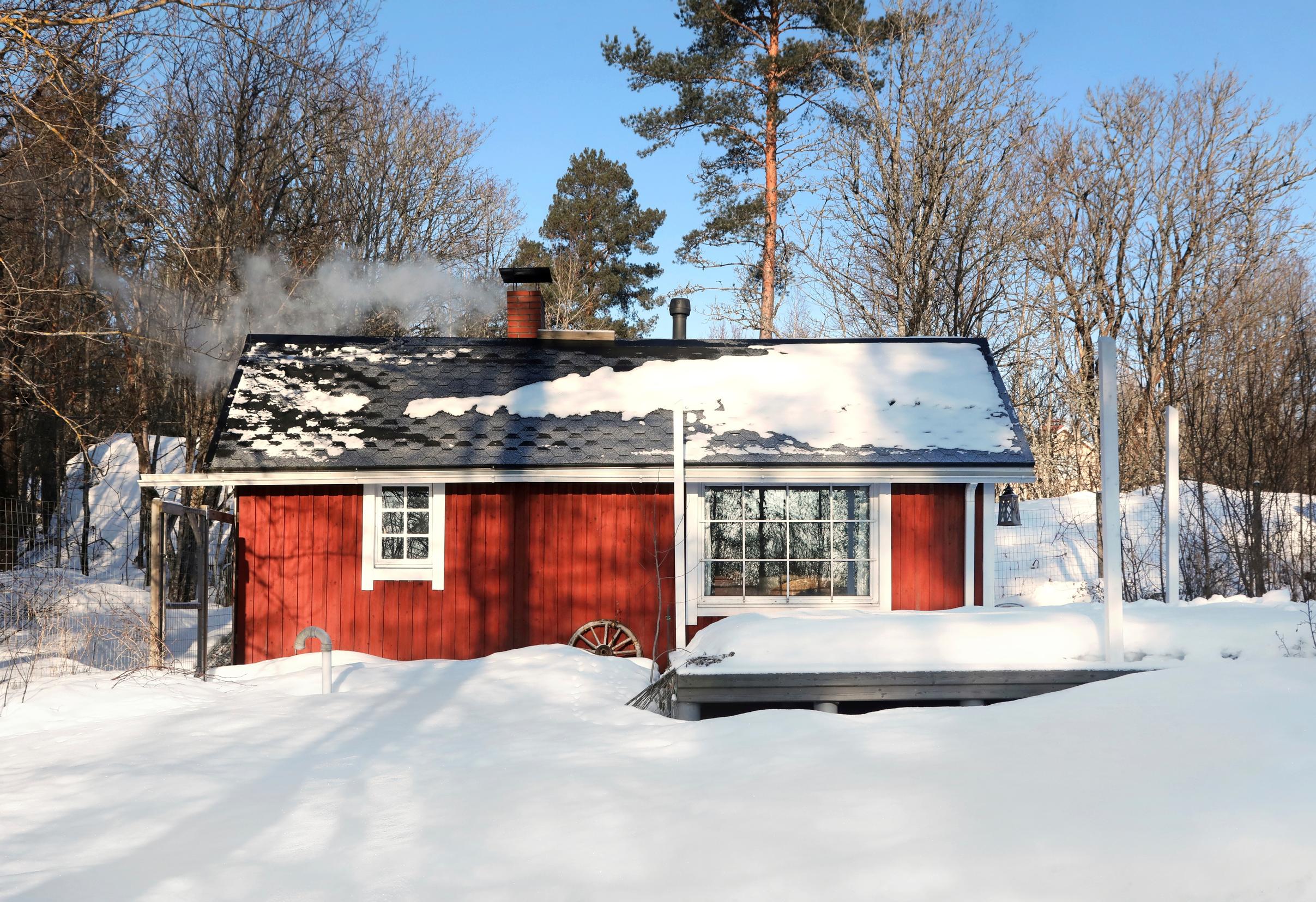 Red garden sauna surrounded by snow, black roof and white window frames