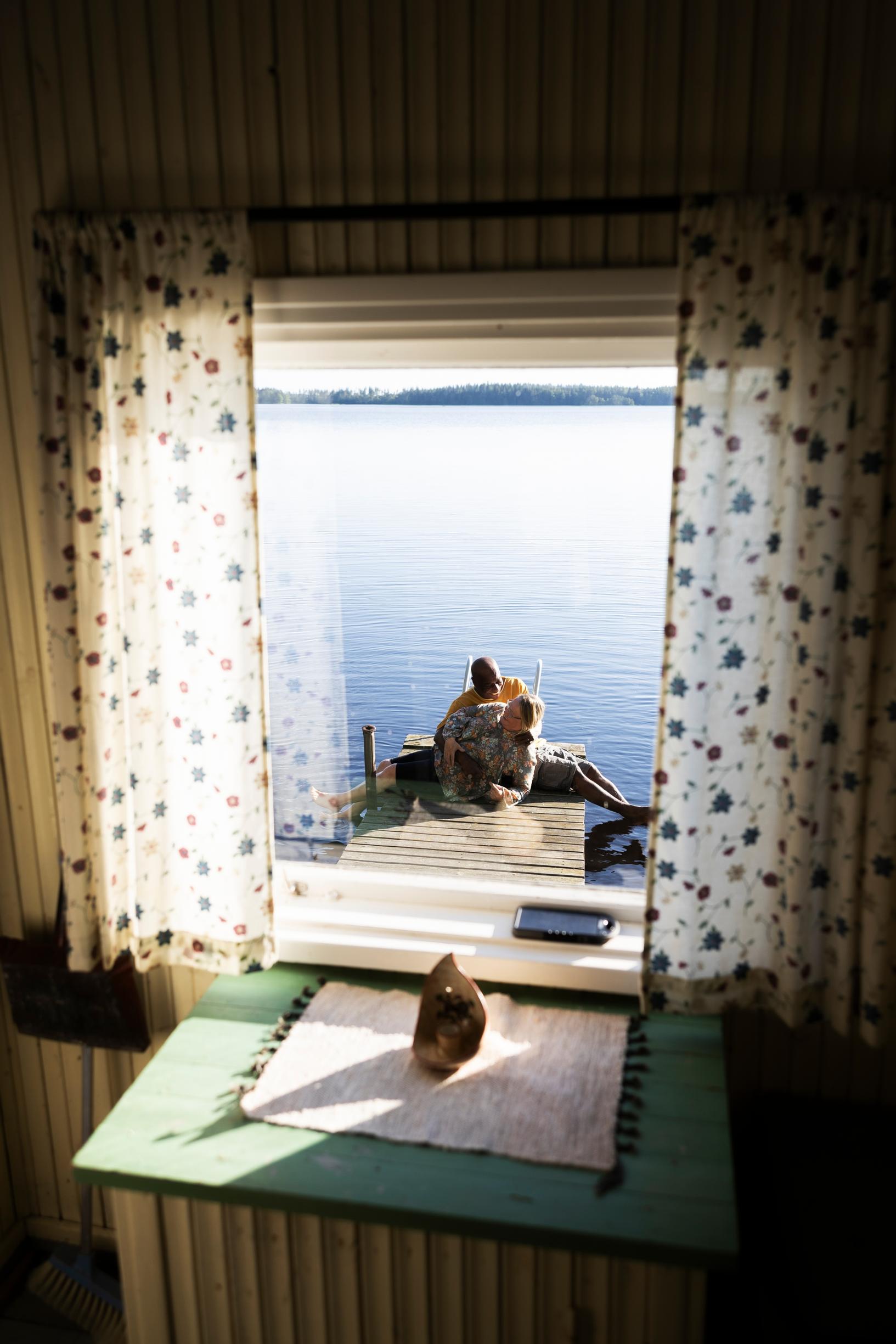 The couple sitting on the dock, view from the window, light summer curtains