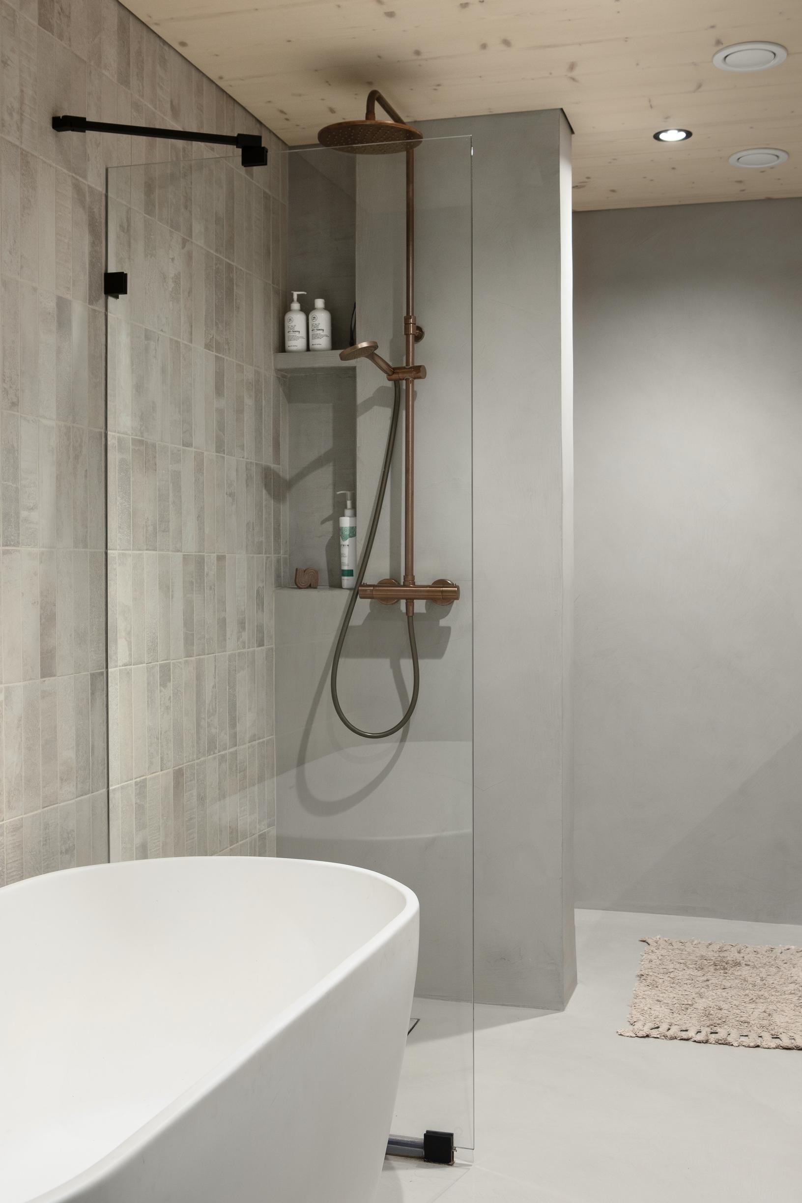 In the bathroom, there is a bathtub and a shower. The floor and walls have microcement.