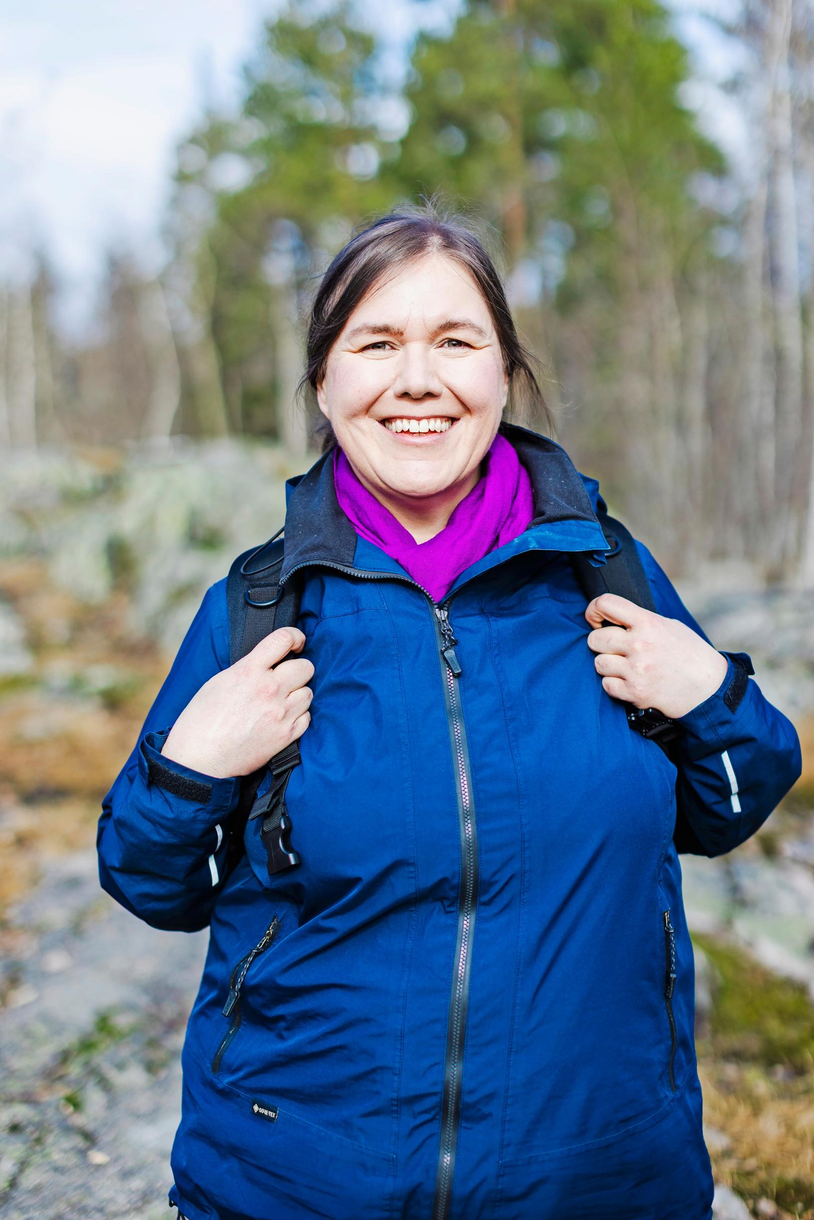 a woman holding her backpack straps and smiling