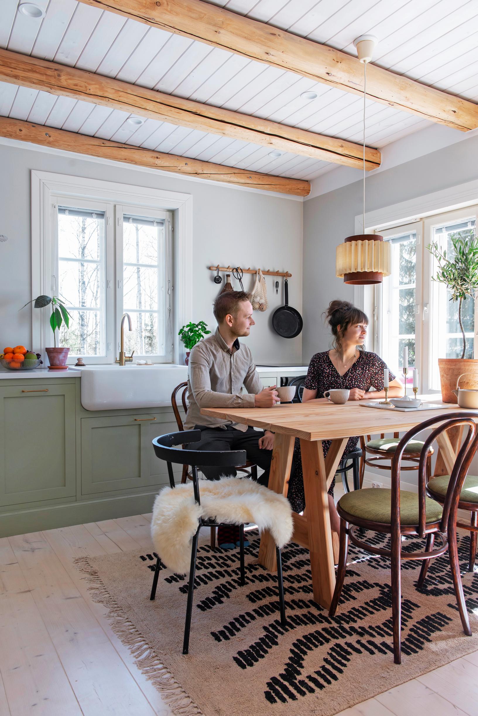 Essi and Valtteri in their green solid wood kitchen with a plank table and Viennese chairs