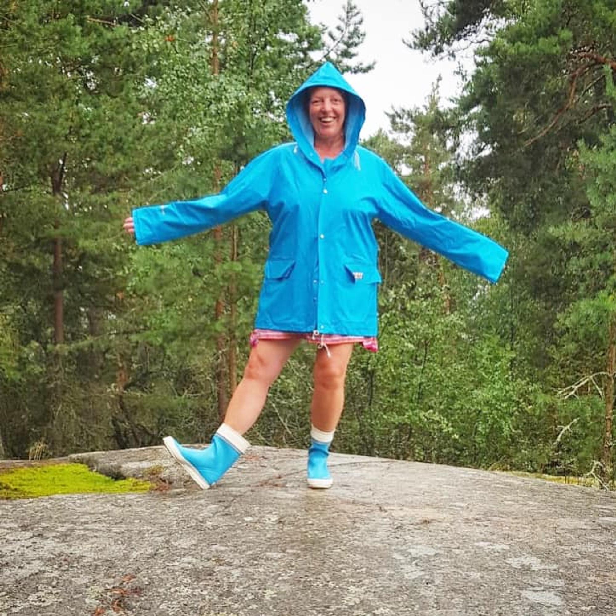 A woman standing on a rock wearing a turquoise raincoat