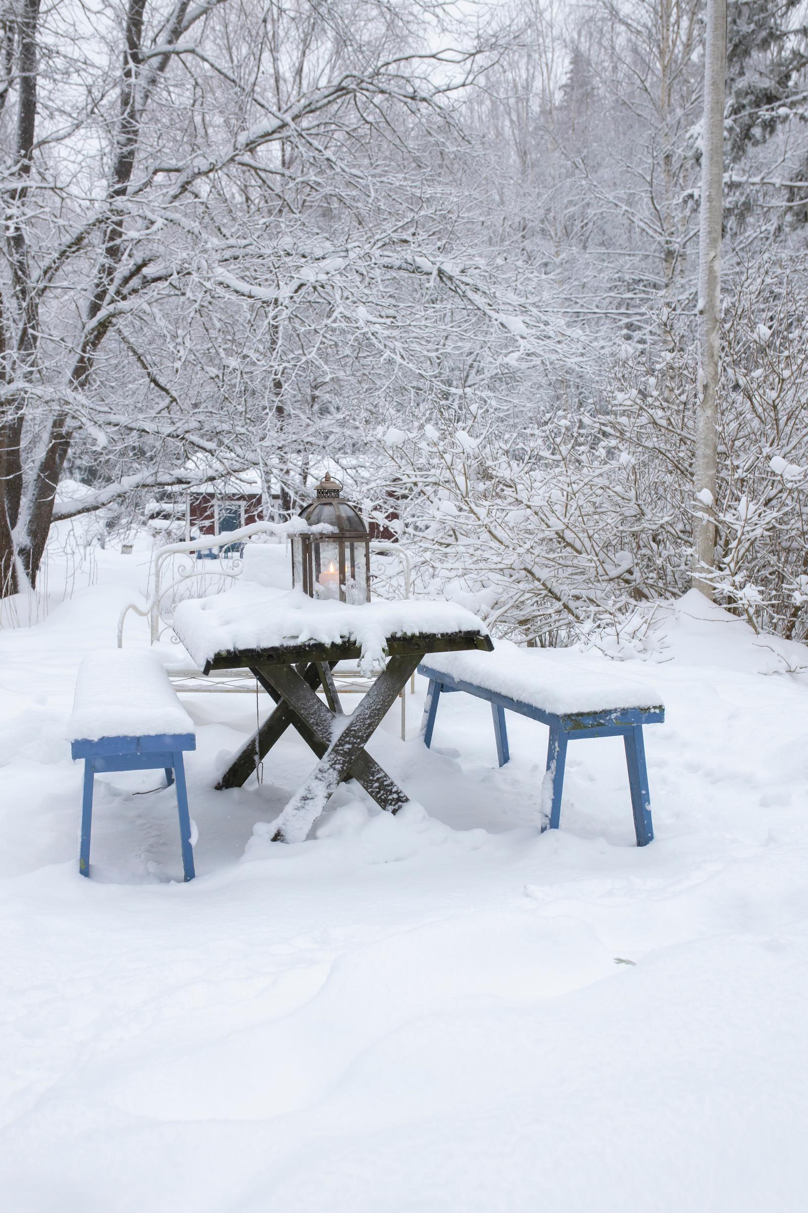 A garden set in the snow with a lantern on the table.