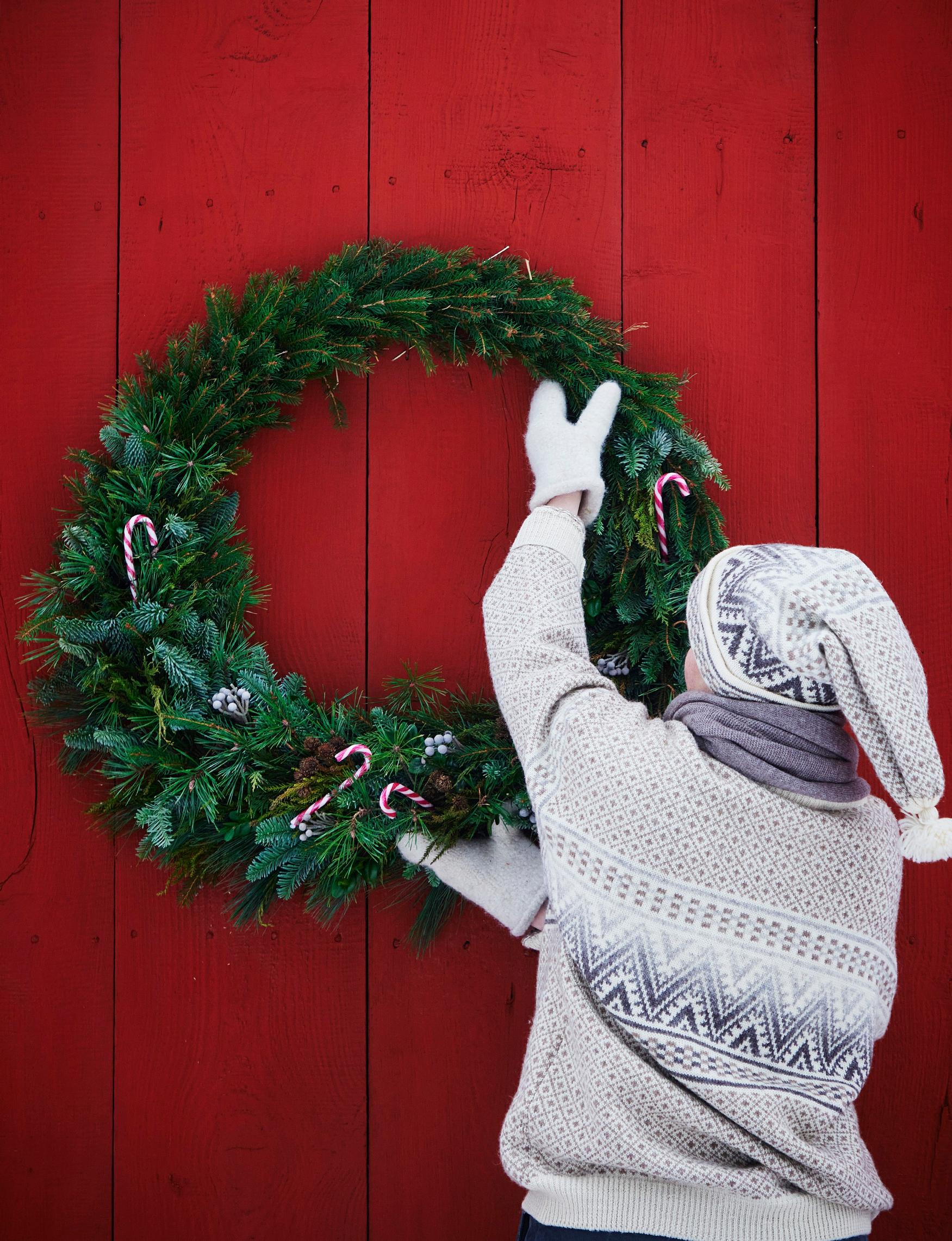 A giant conifer wreath hung on a red wooden wall.