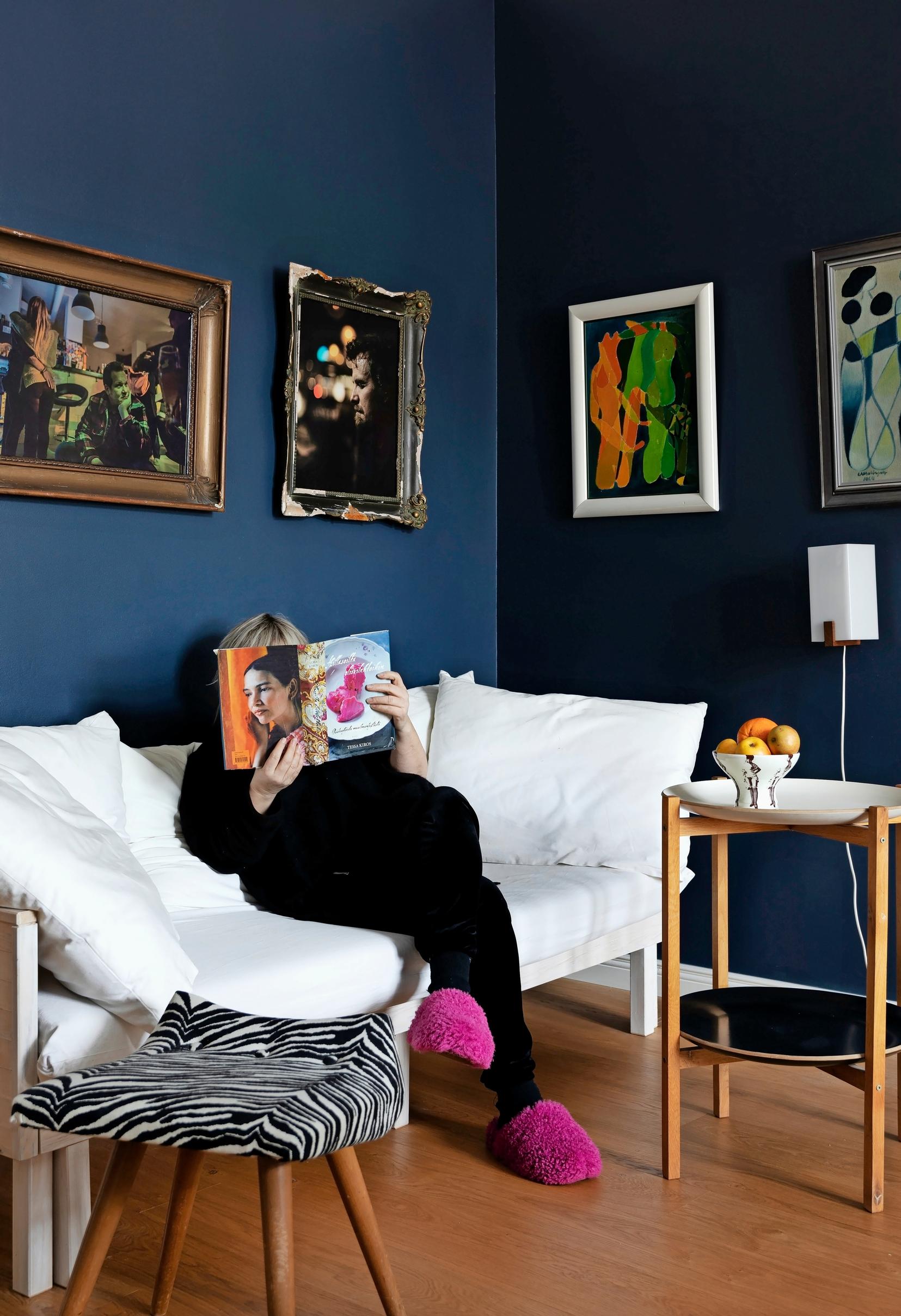 A woman reading on a white sofa. There are several artworks on the walls.