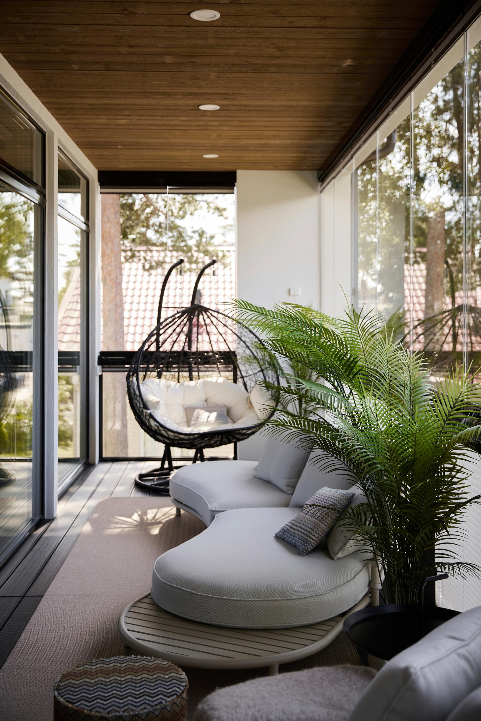 A glassed-in balcony with outdoor furniture and a palm.