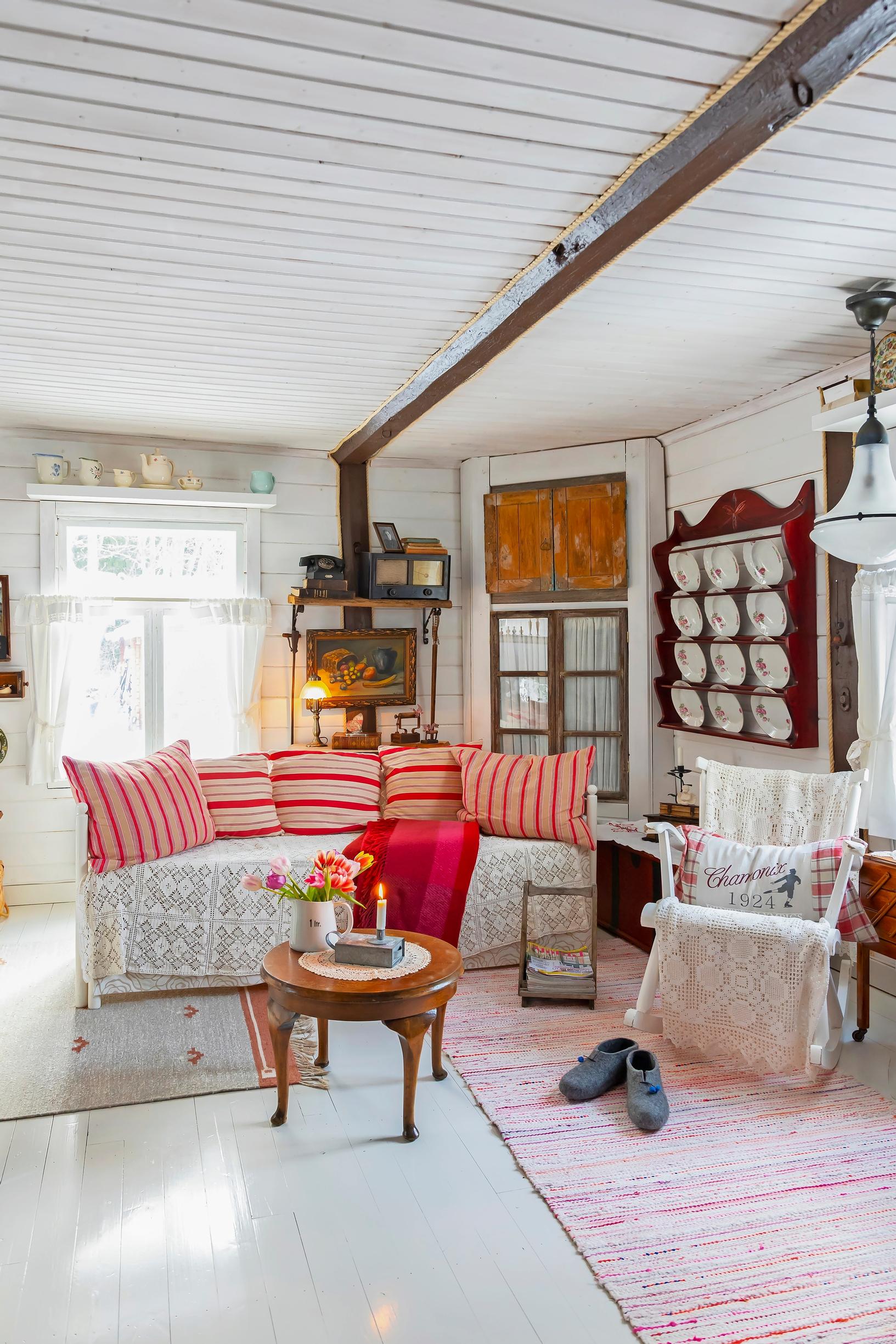 in the cottage living room, a sofa with red-striped cushions, a china cabinet, a rocking chair, and a rag rug