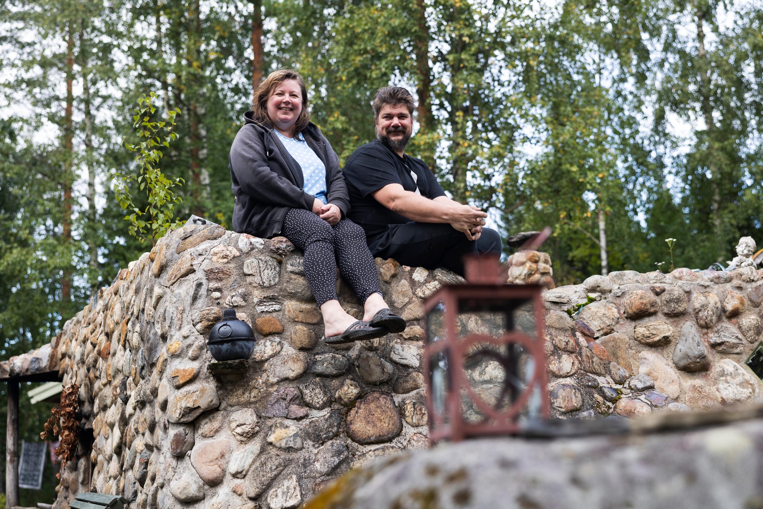 Anne and Juha Turunen sitting on the roof of the smoke sauna built from natural stones, smiling.