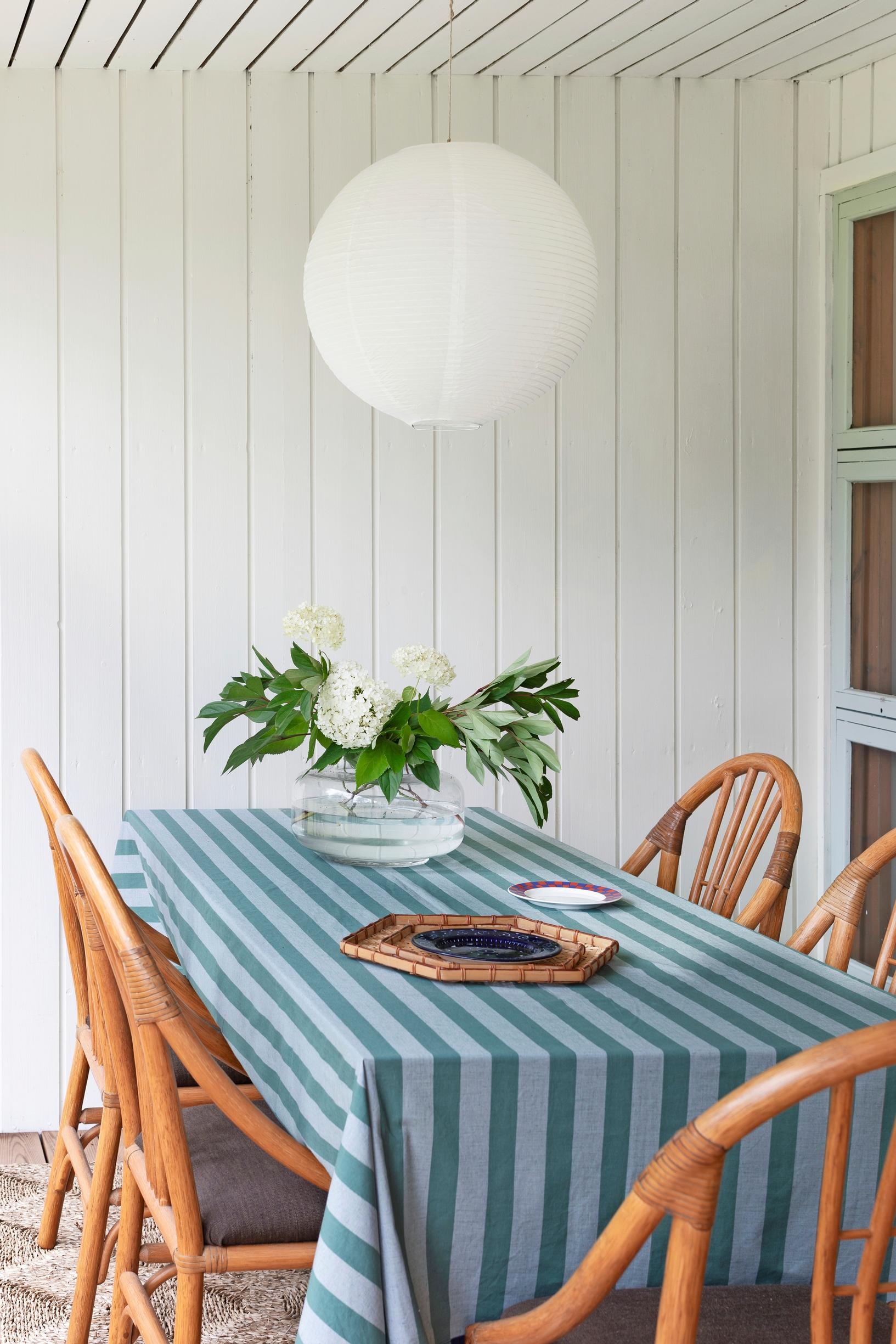 A striped tablecloth and rattan chairs around the table, flowers in a vase.