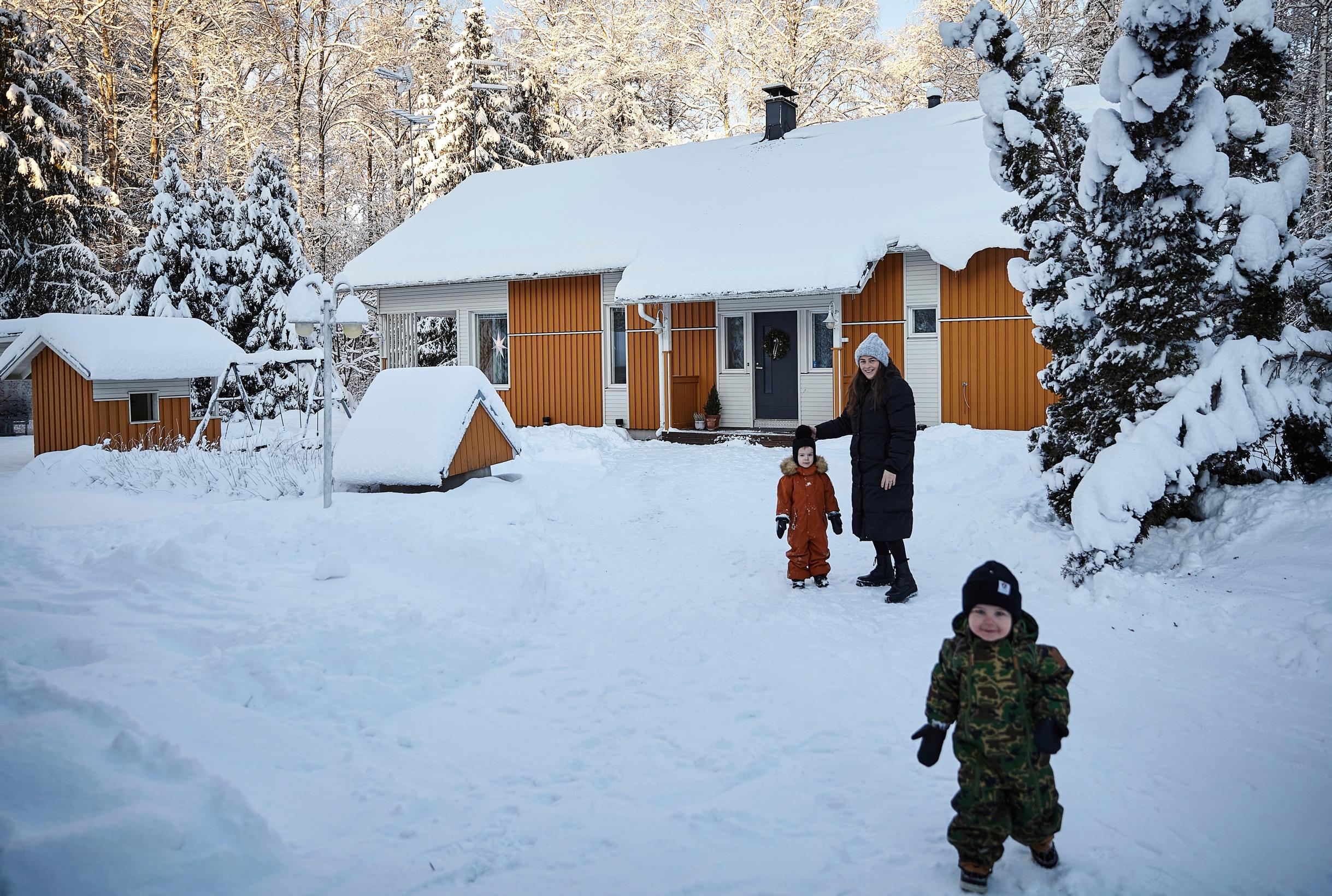 A mother and two children in front of a yellow house, standing in a snowy yard