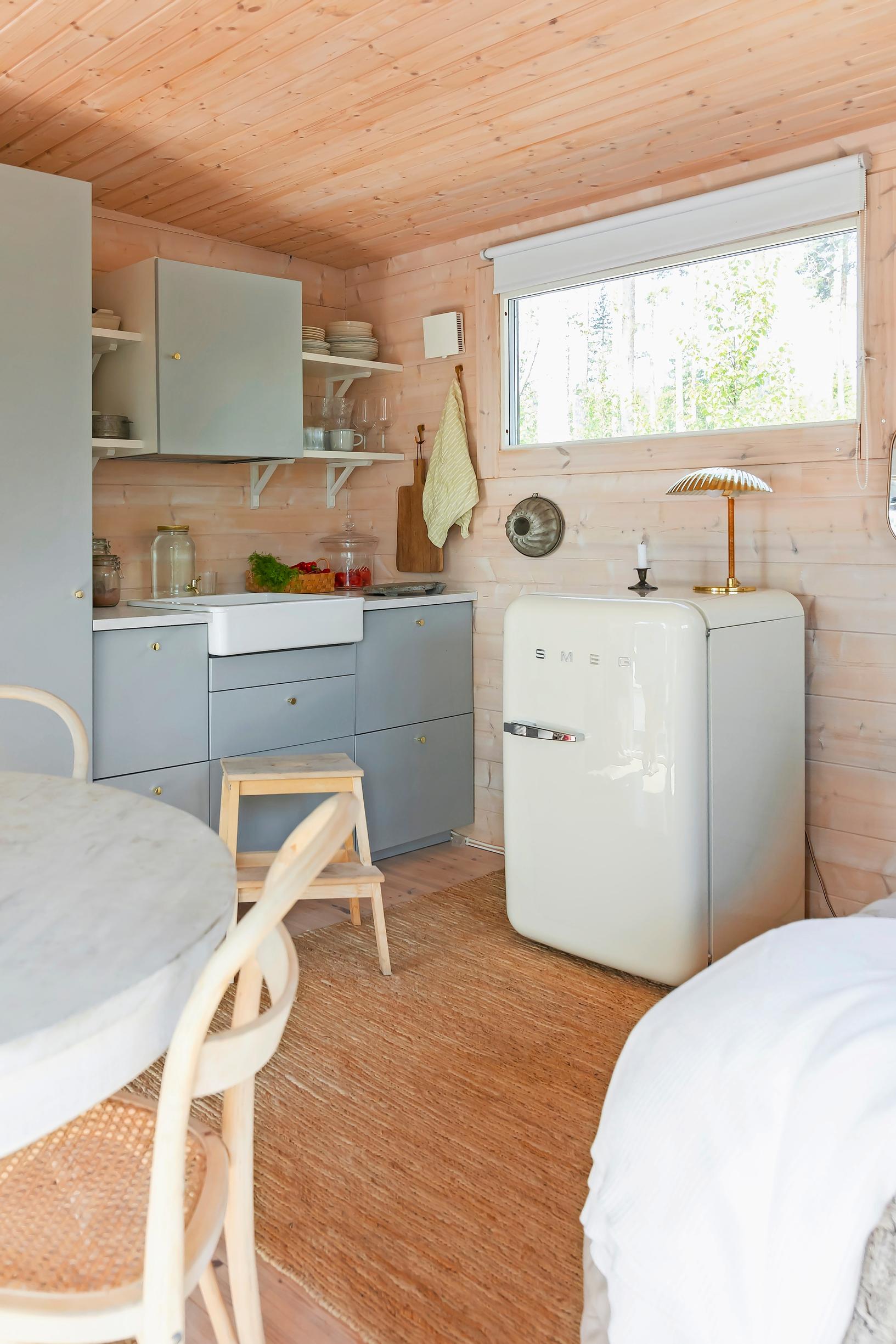 blue-gray kitchen cabinets and a small white fridge in the kitchen, part of a dining set, and a small window