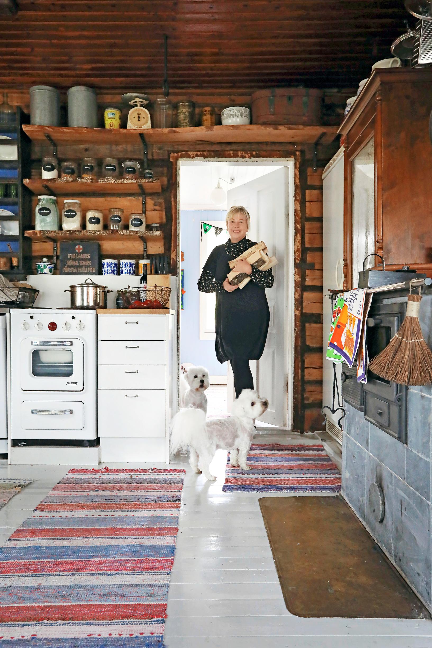 Nina at the kitchen door of the log house, with a dog at her feet.