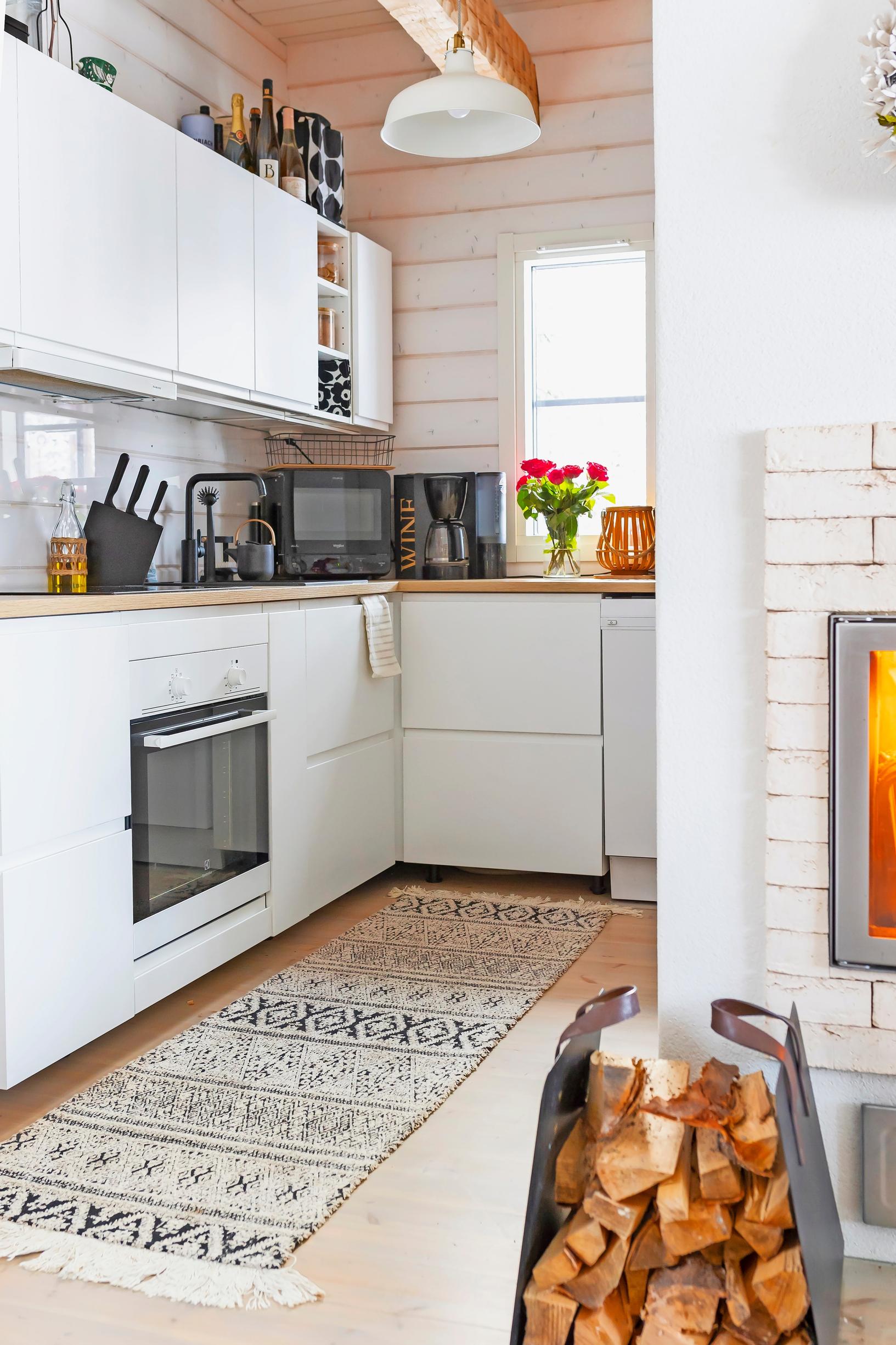 White kitchen, colorful rug, and fireplace with fire and log holder