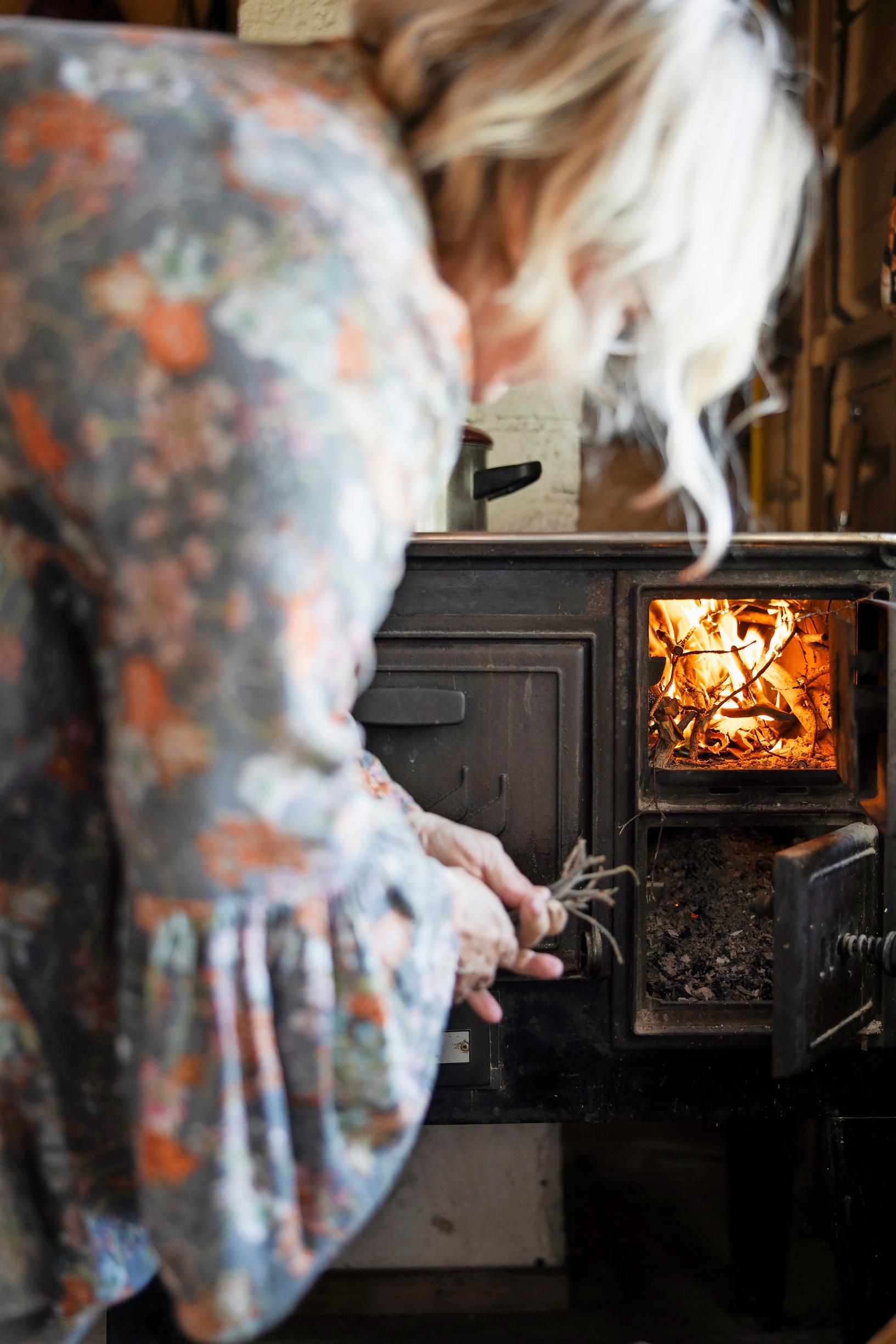 Adding twigs to the wood stove’s firebox