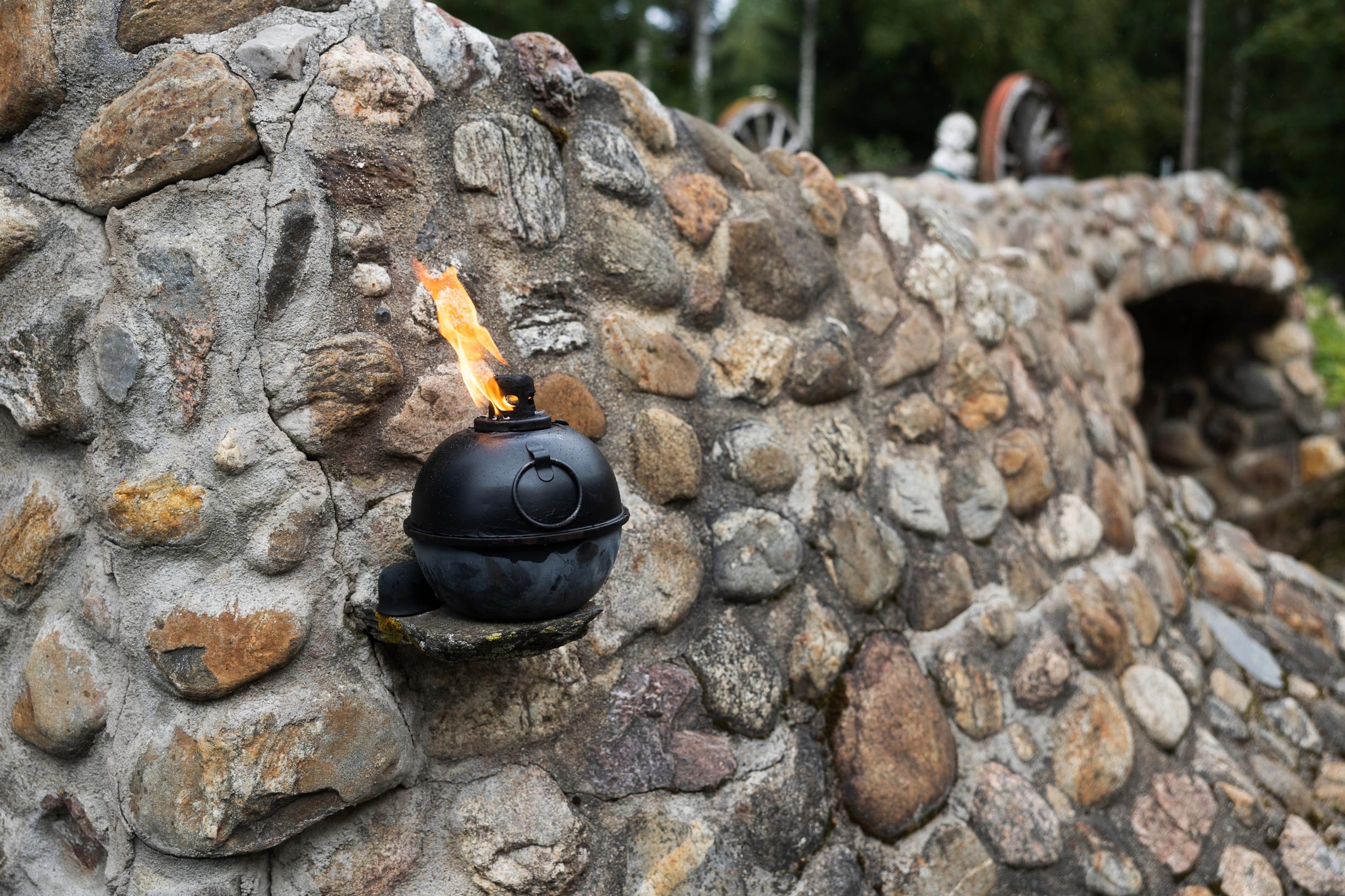 A flame rising from a kettle attached to a wall built of natural stones