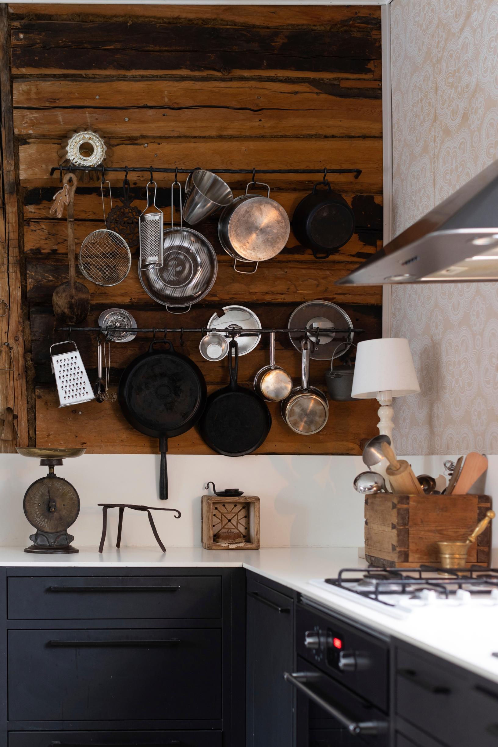 A modern black lower cabinet with a white countertop against a dark log wall adorned with beautiful hanging pots.