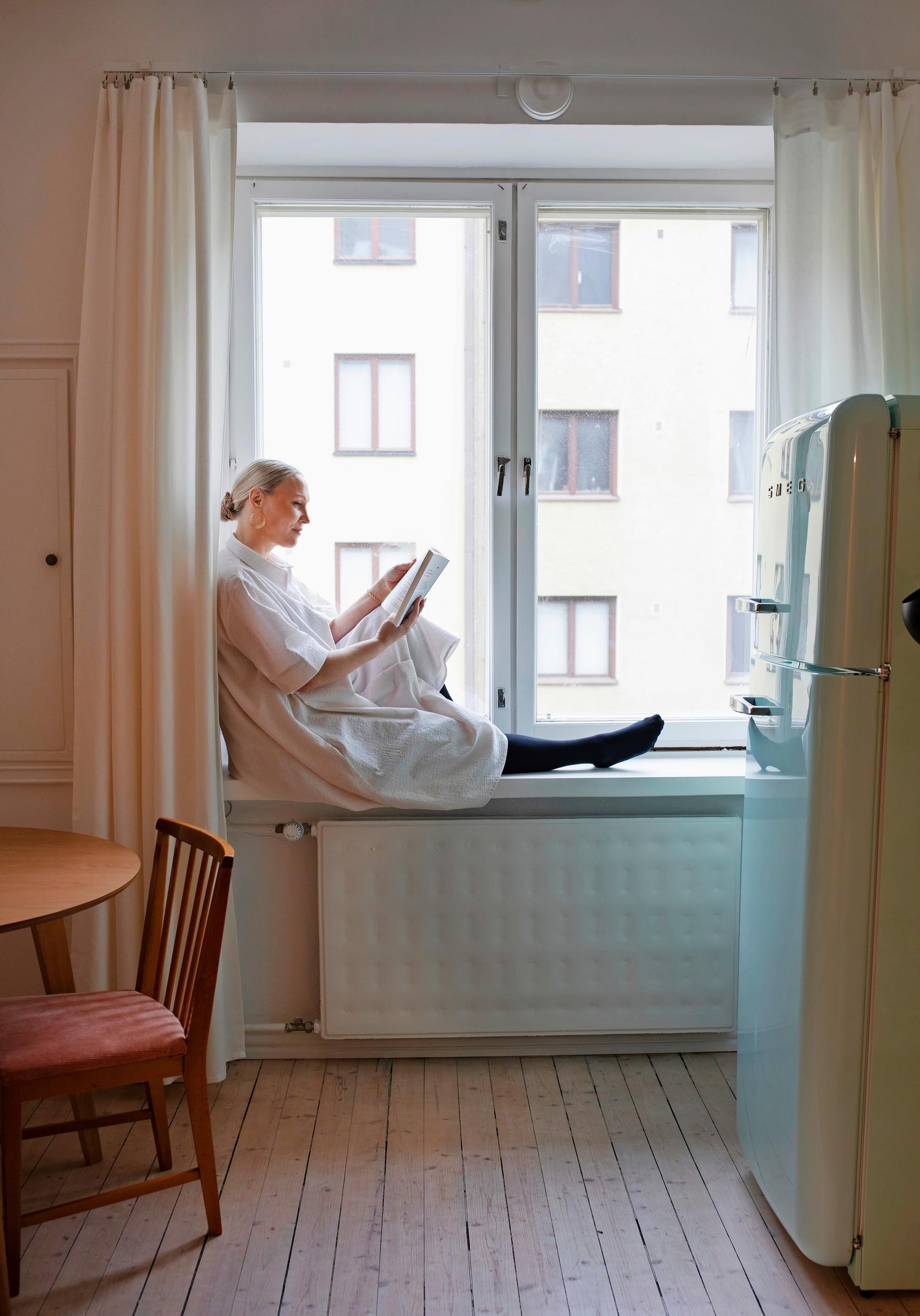 Photo of Kati Jukarainen sitting on a windowsill reading a book.