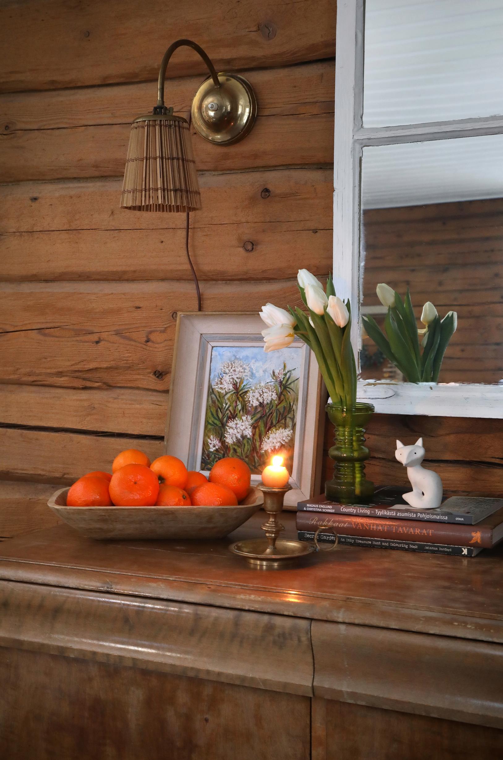 In the log cabin, a small painting sits atop a sideboard, along with tulips, a candle, and mandarins.