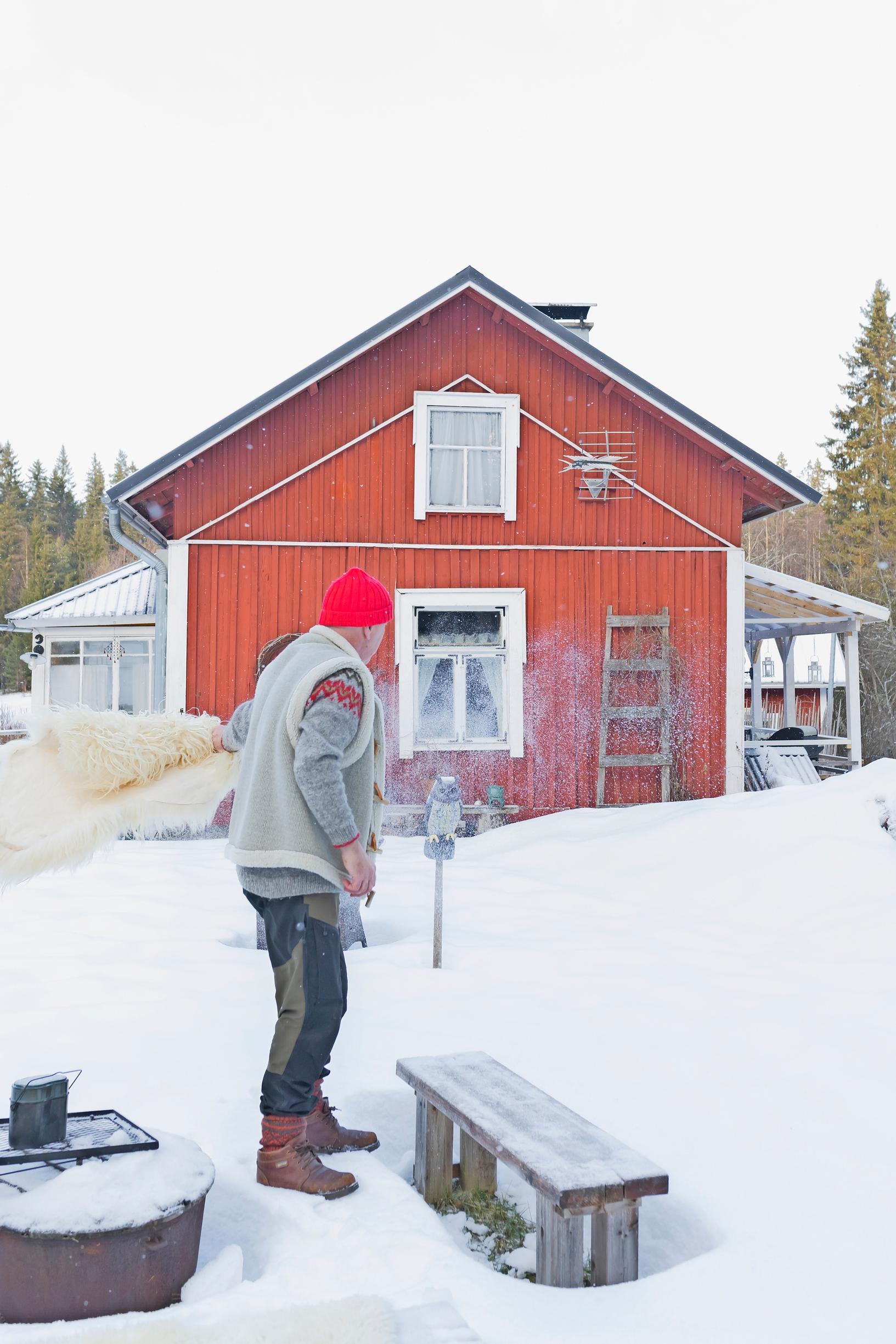 a man stands at a snowy grill spot with a red cottage in the background