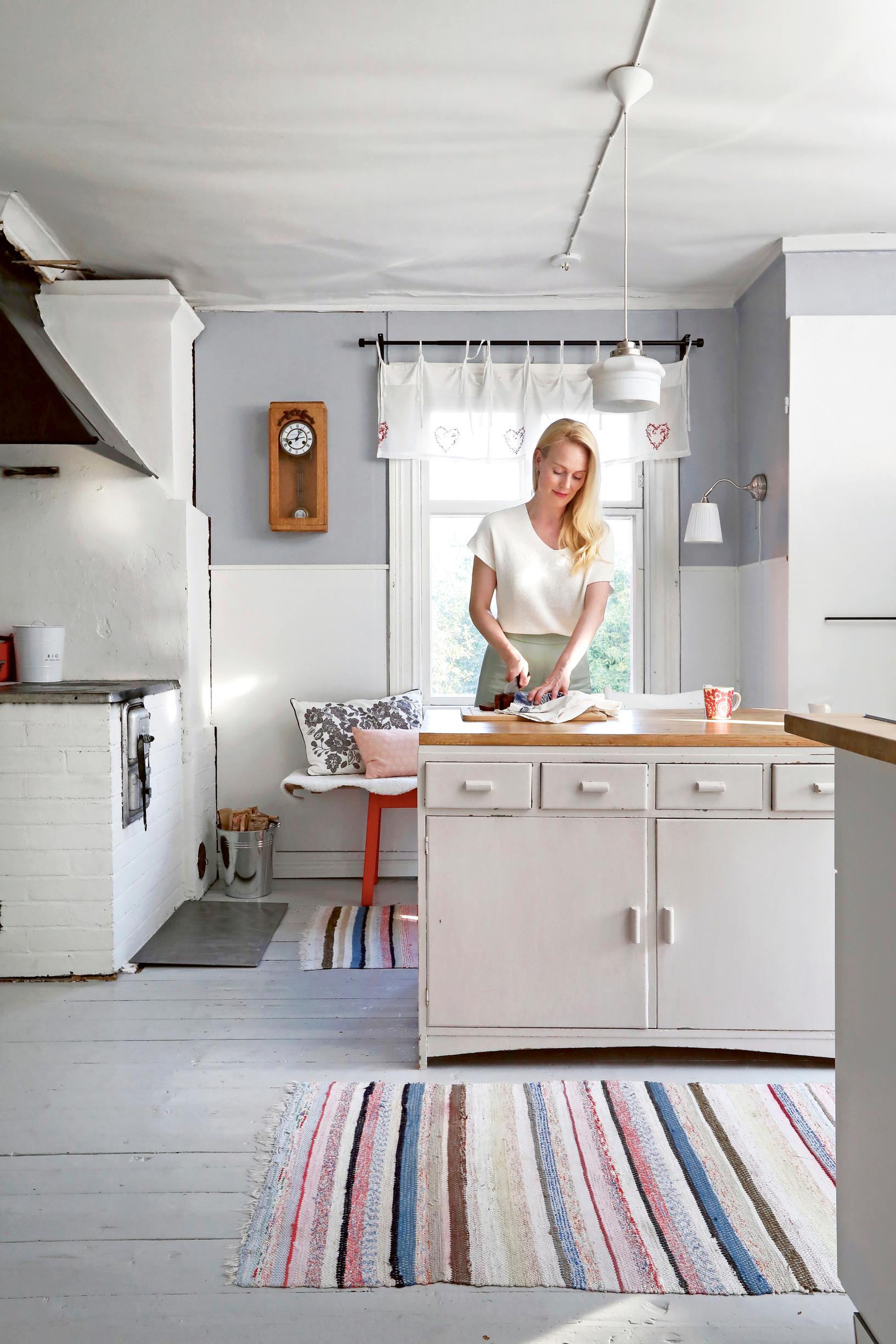 Jutta Helenius preparing food on the sideboard that serves as a kitchen island, rag rug, and wood stove
