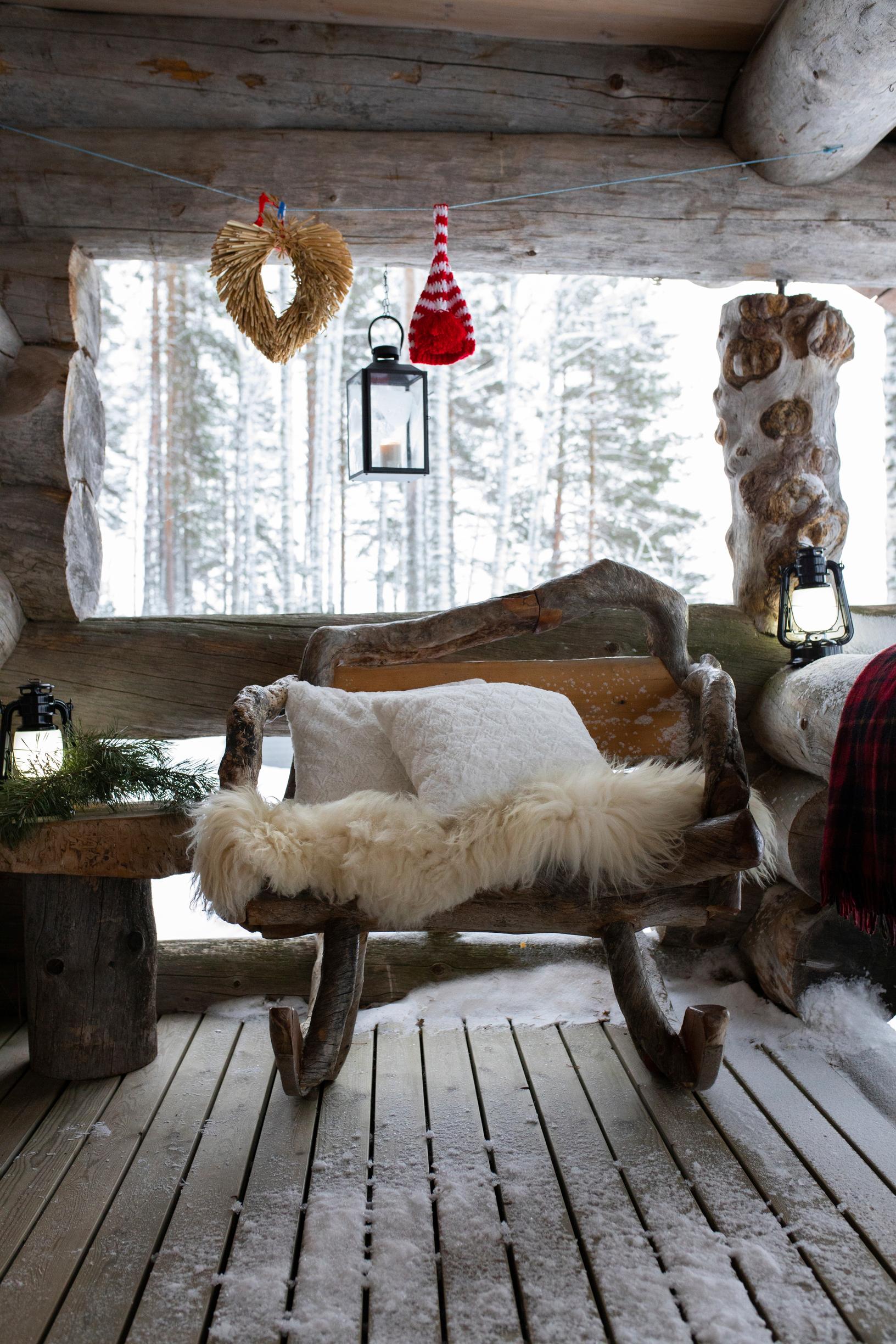 A rocking bench made of kelo wood stands on the snowy cabin terrace, draped with a sheepskin.