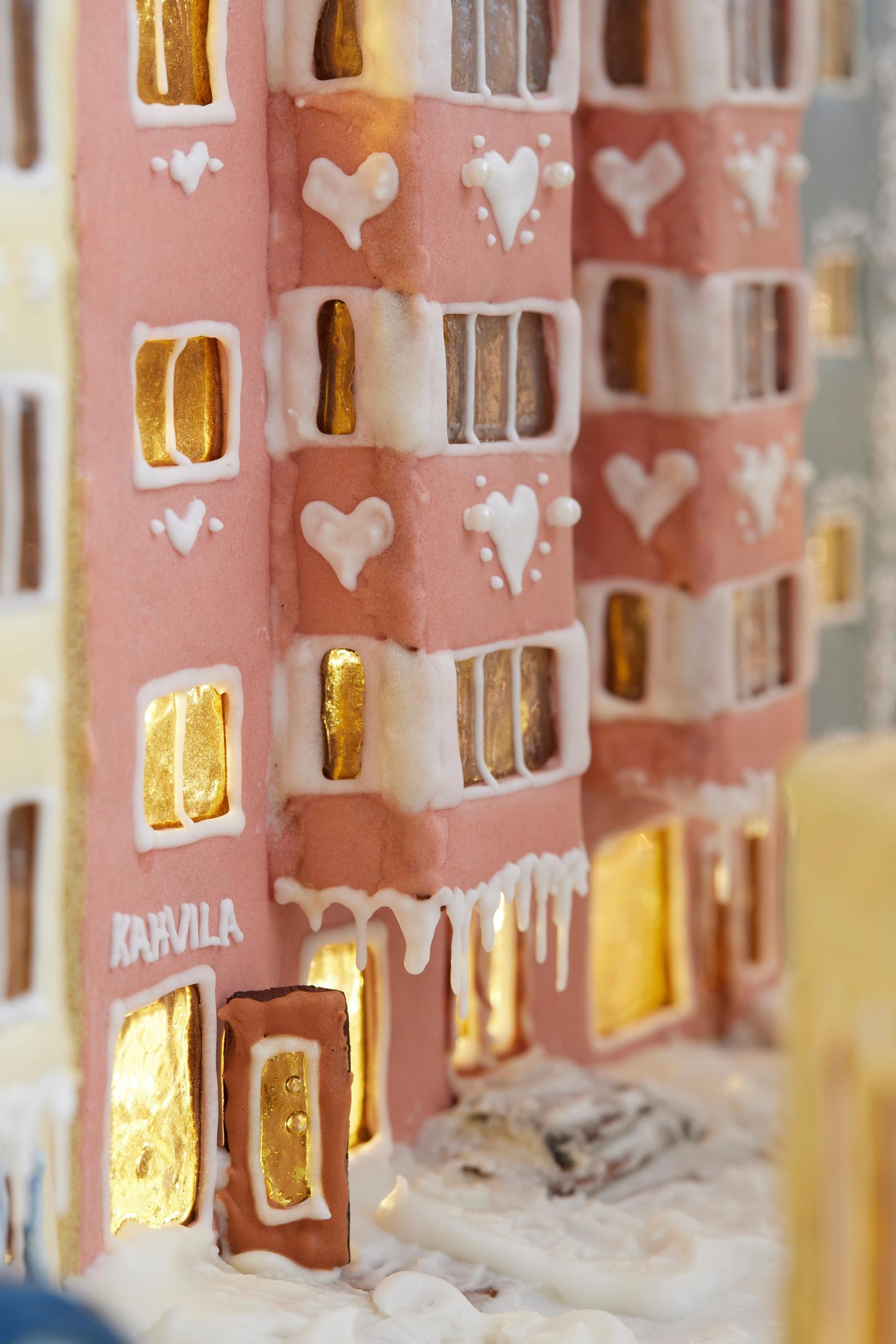 A gingerbread city block featuring a 1950s apartment building with bay windows covered in pink royal icing.