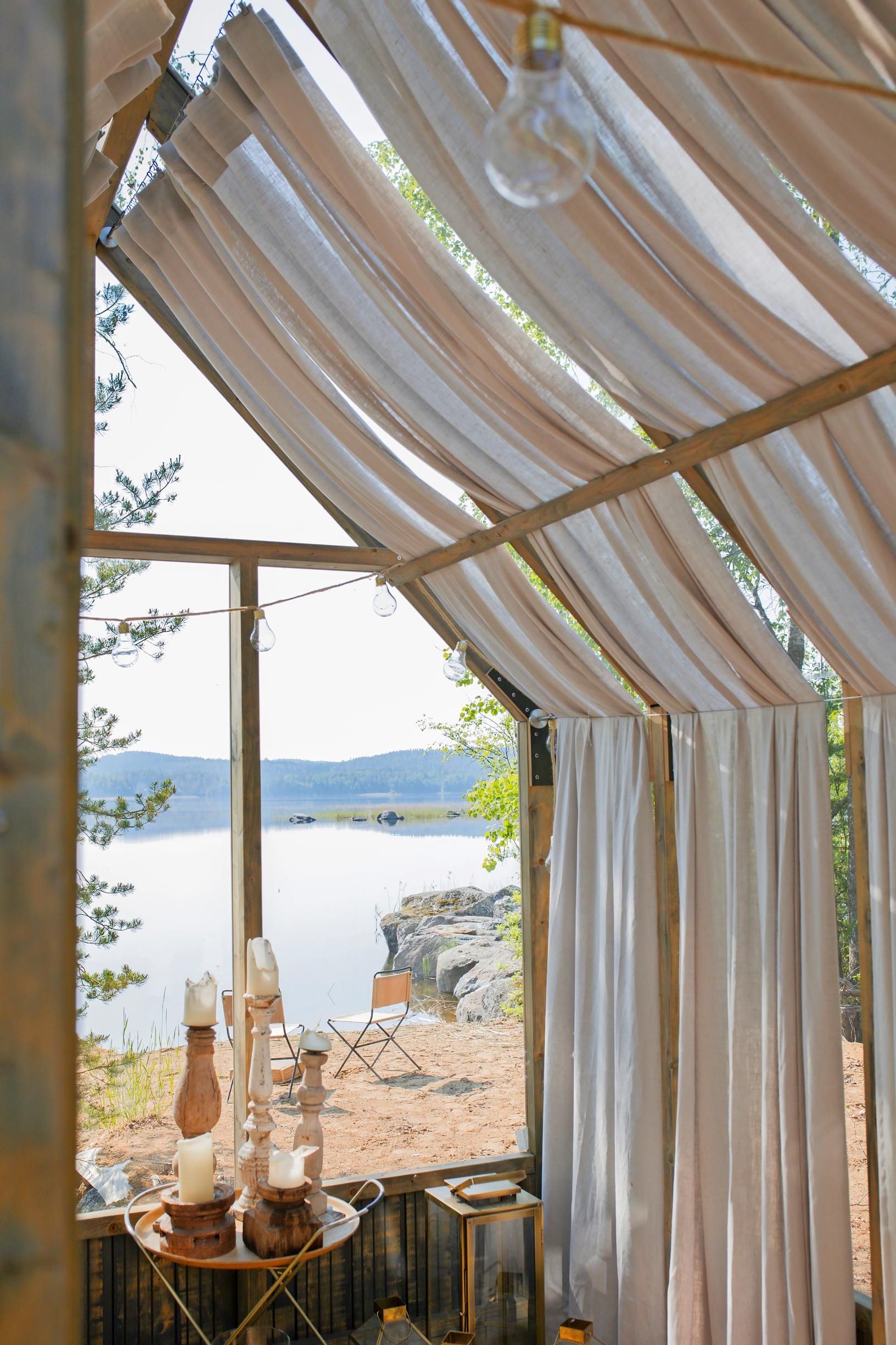 long curtains on the greenhouse roof and walls, a small table, and a lake view