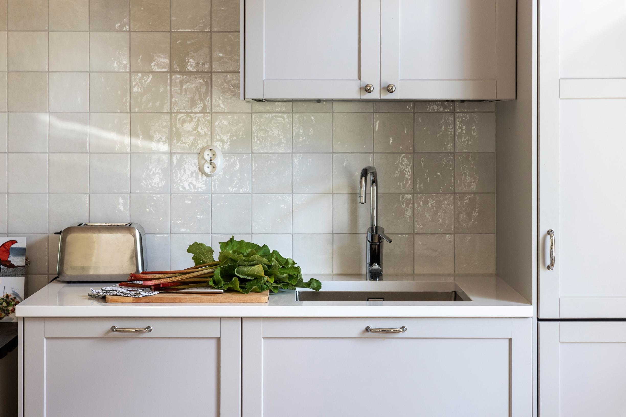 Gray kitchen cabinets with white pearl-toned square tiles in the backsplash