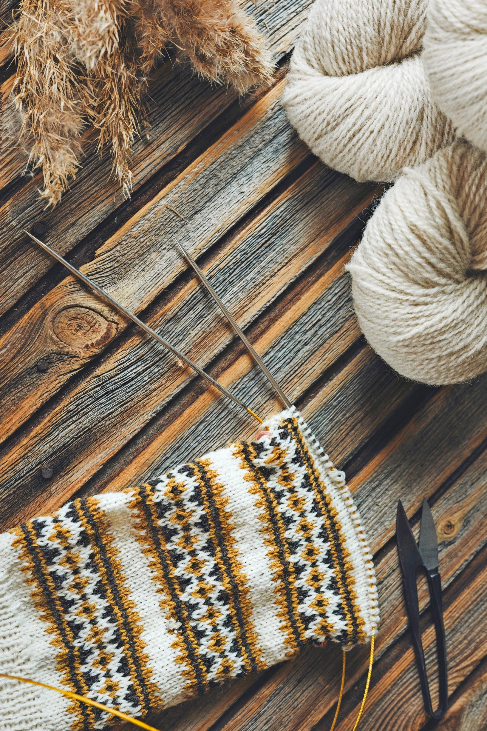 A stranded project on the needles in white, straw yellow, and blue.