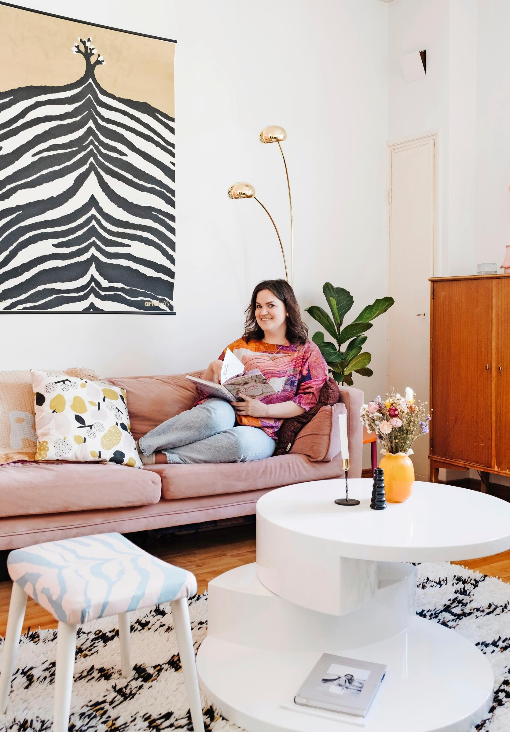 Photo of a woman in her living room on a pink sofa reading a book.