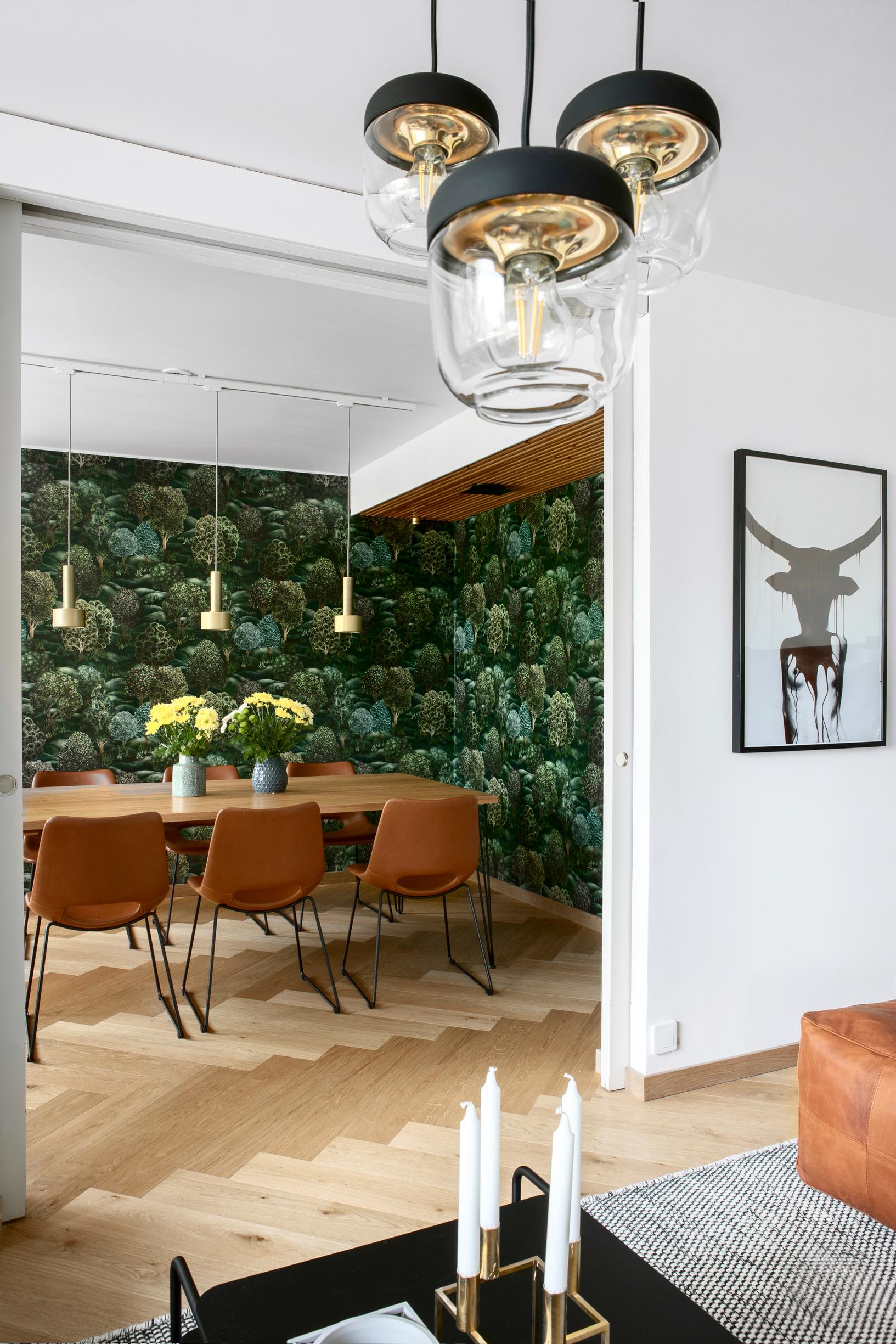 Two walls of the room are wallpapered with green-toned wallpaper. In the center of the space is a dining set.
