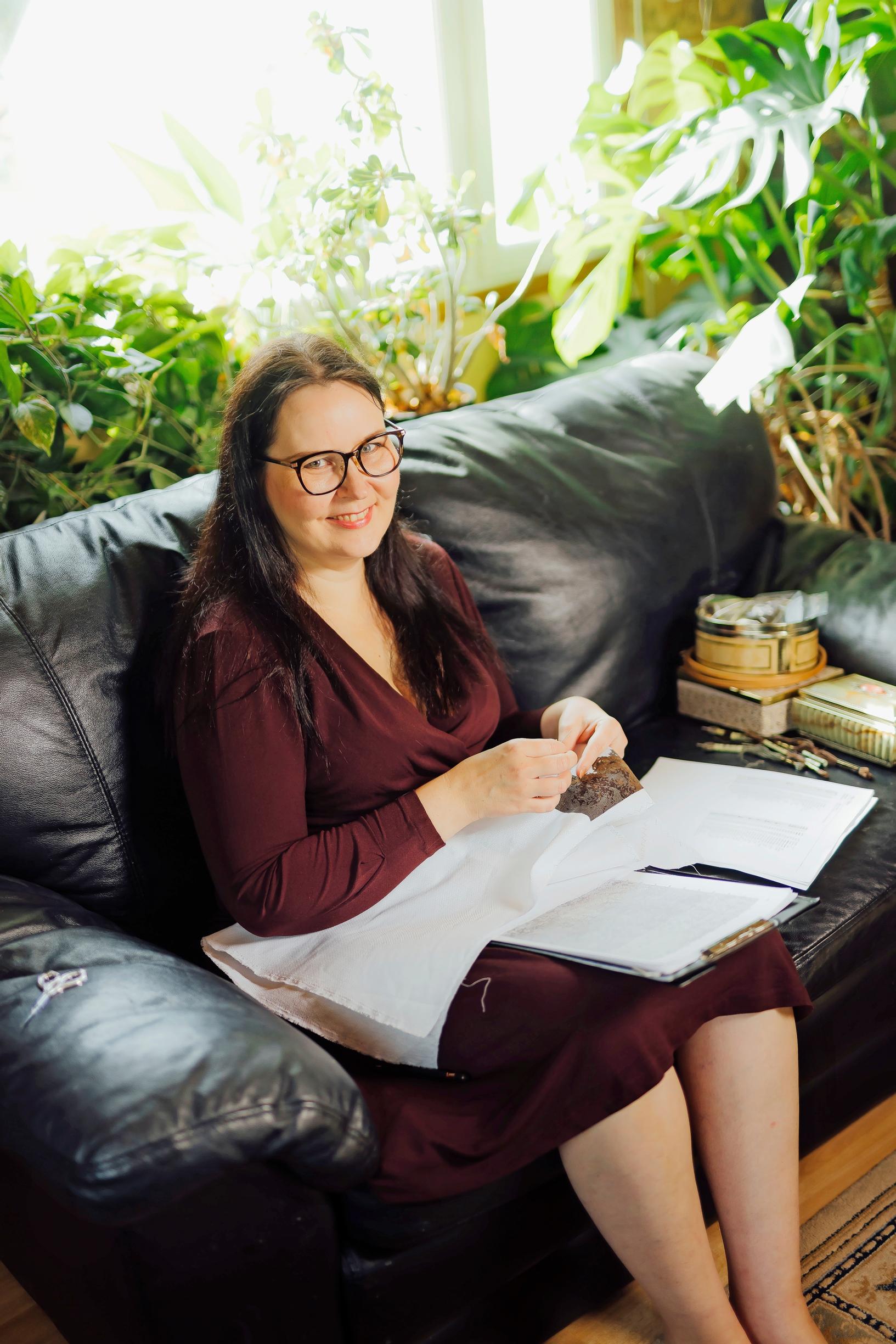 Tanja sits on a sofa with a cross-stitch piece in her lap.