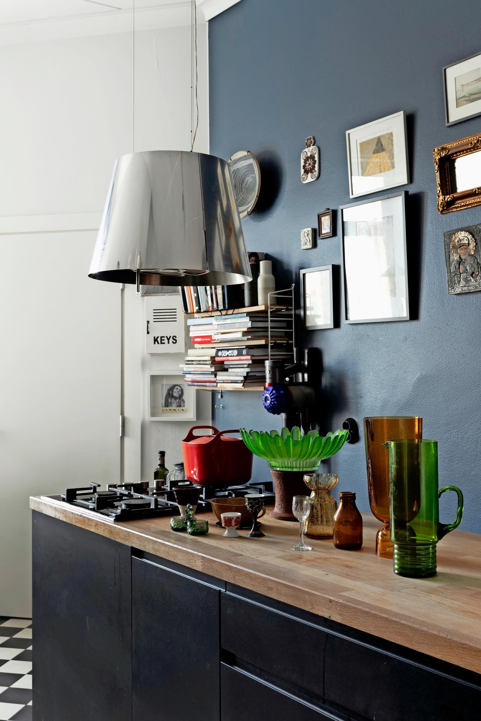 Kitchen. The image shows a countertop and stove. On the wall are paintings and a shelf with books.