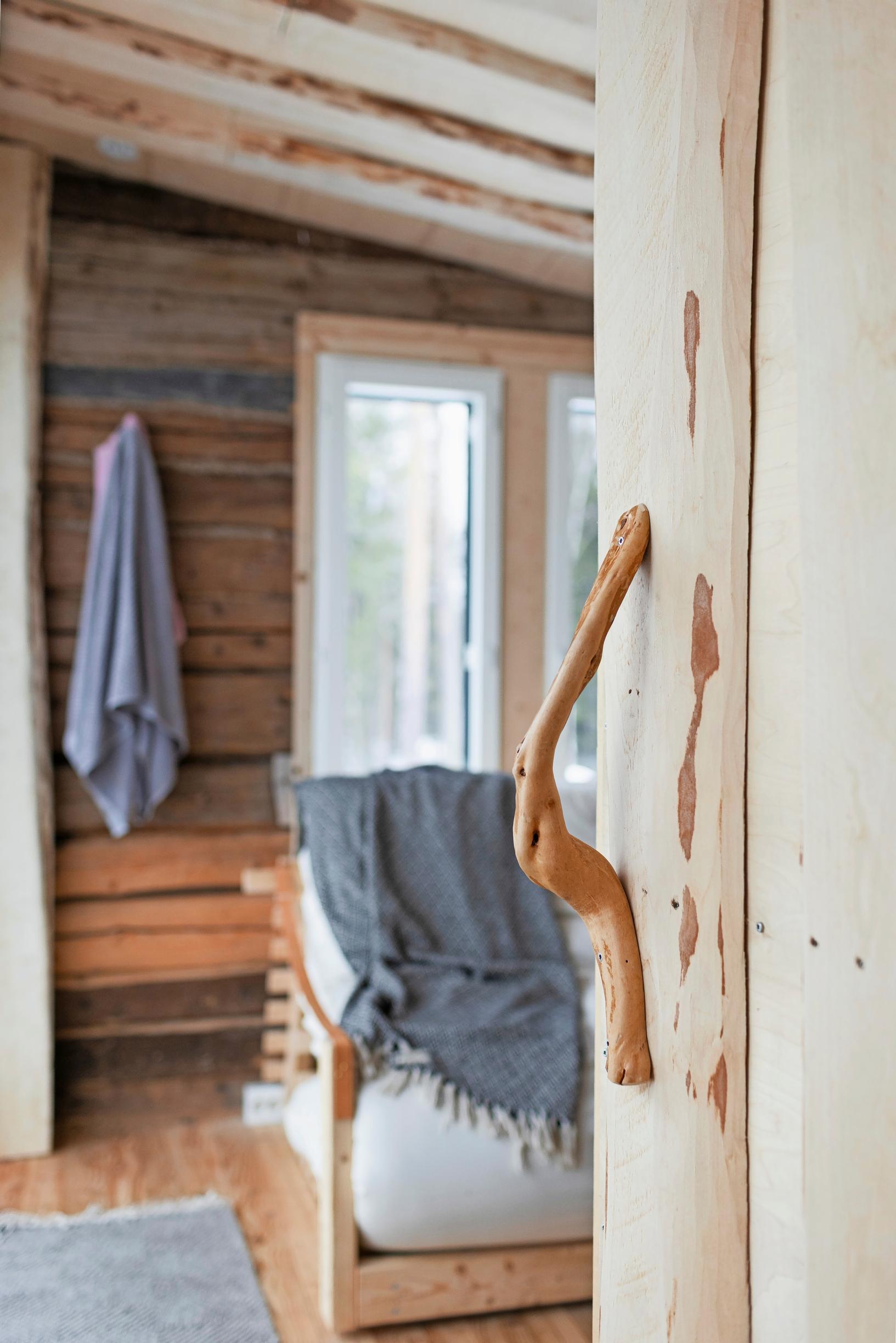 A wooden handle on a wooden door, with a blanket on the sofa in the background.