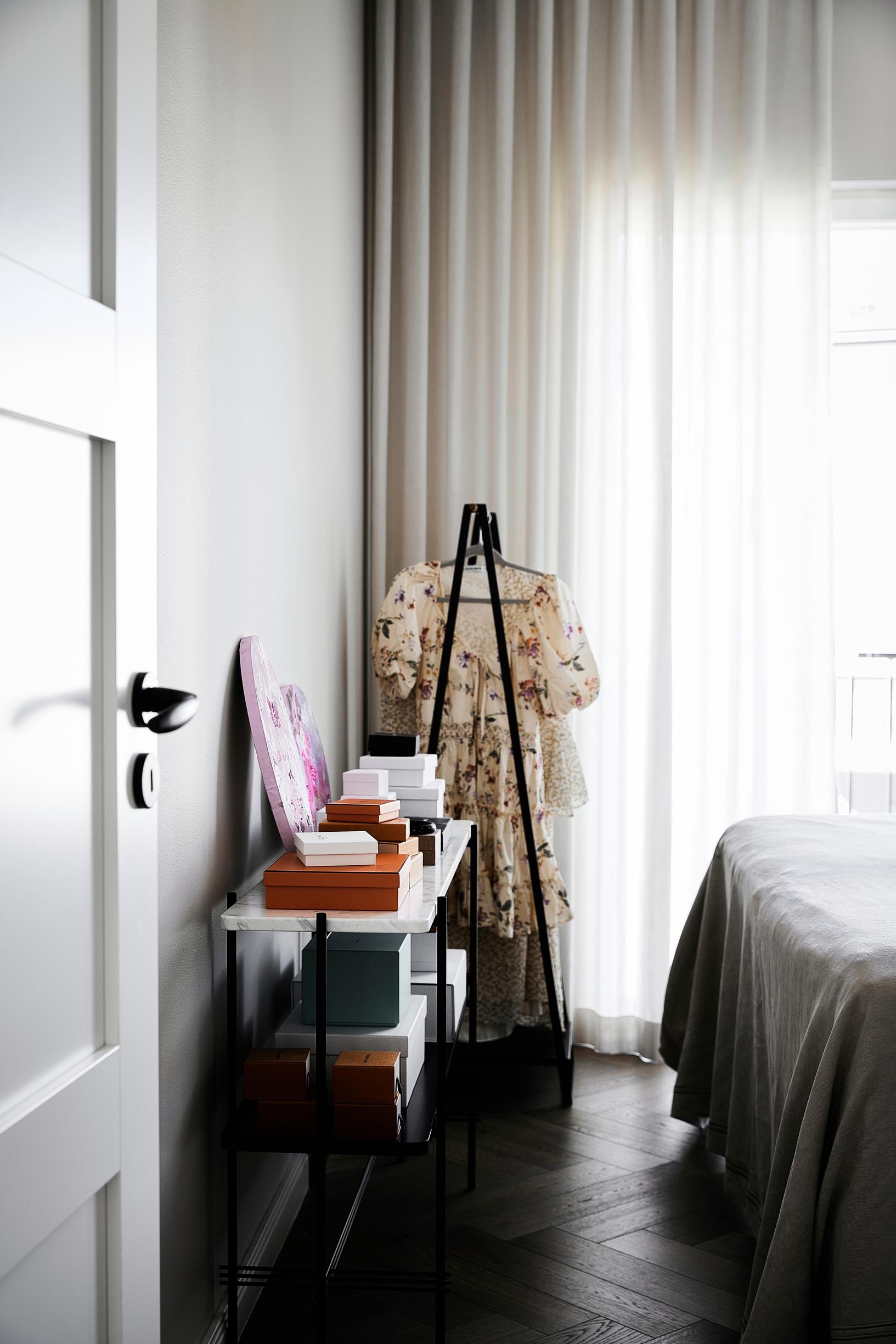 A corner of the bedroom with a side table and clothing rack.