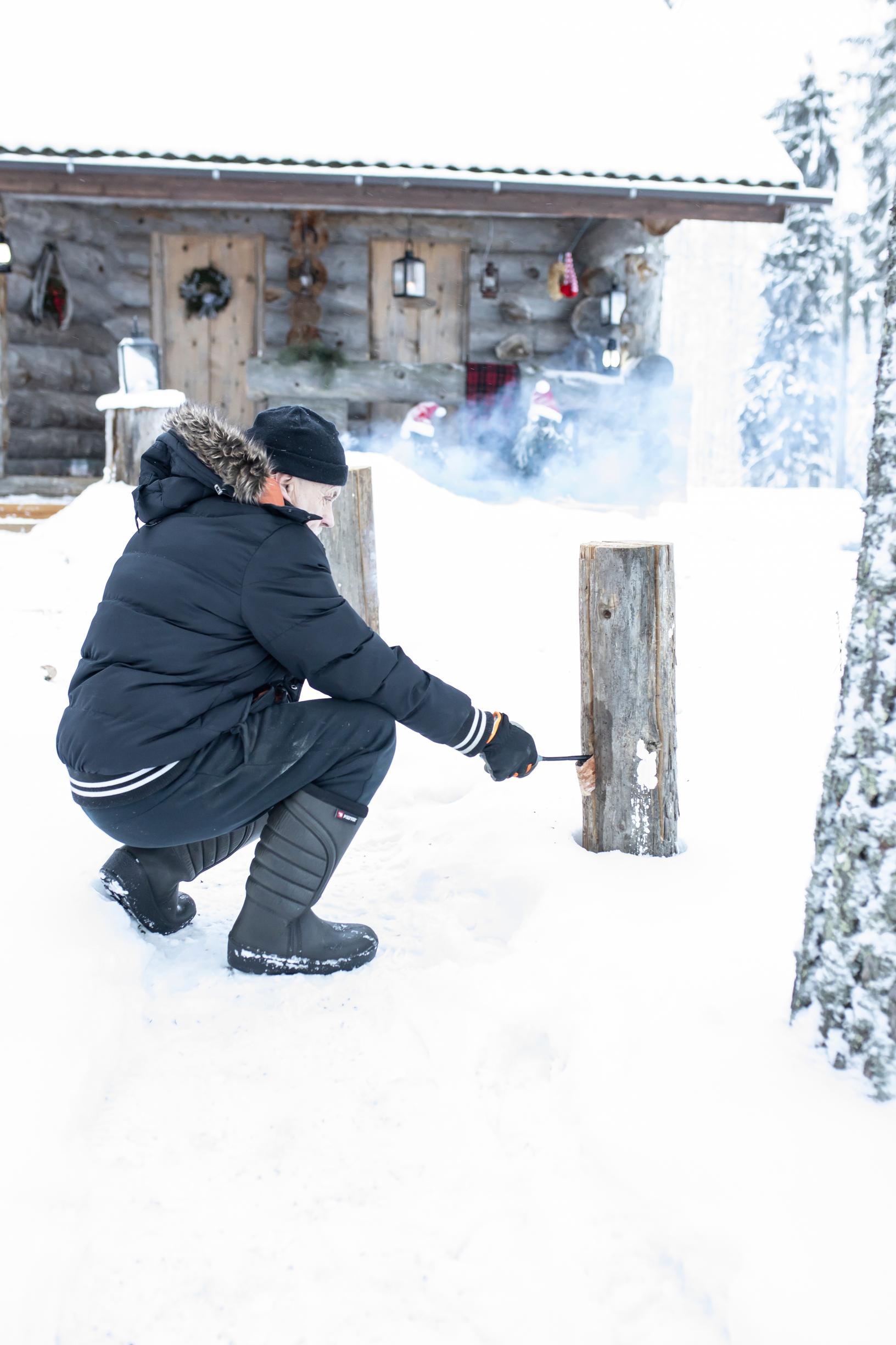 A man lights log torches in the snow in front of the kelo cabin.