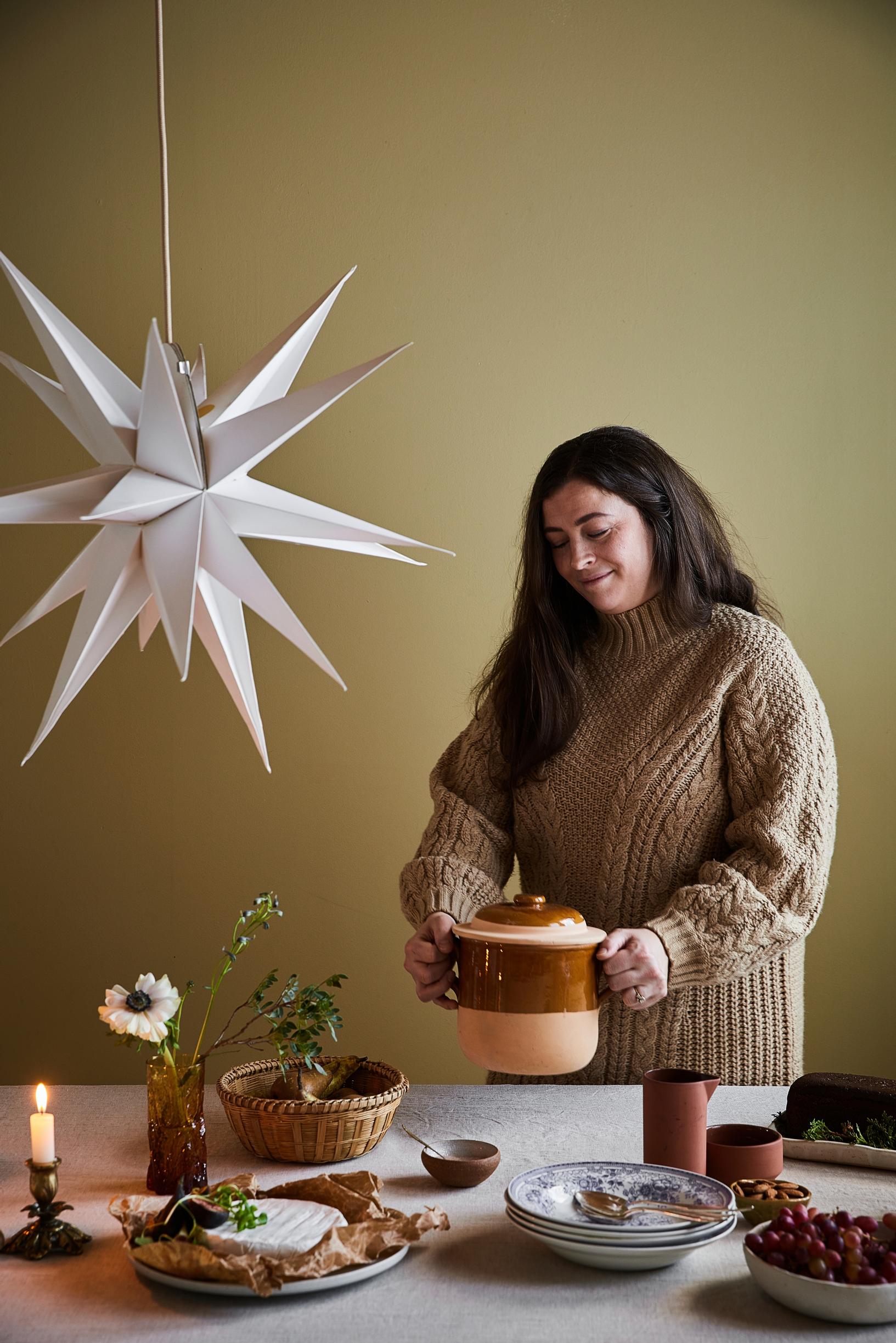 Jade Anetjärvi lifts a ceramic dish from a set table, with a white Christmas star above the table