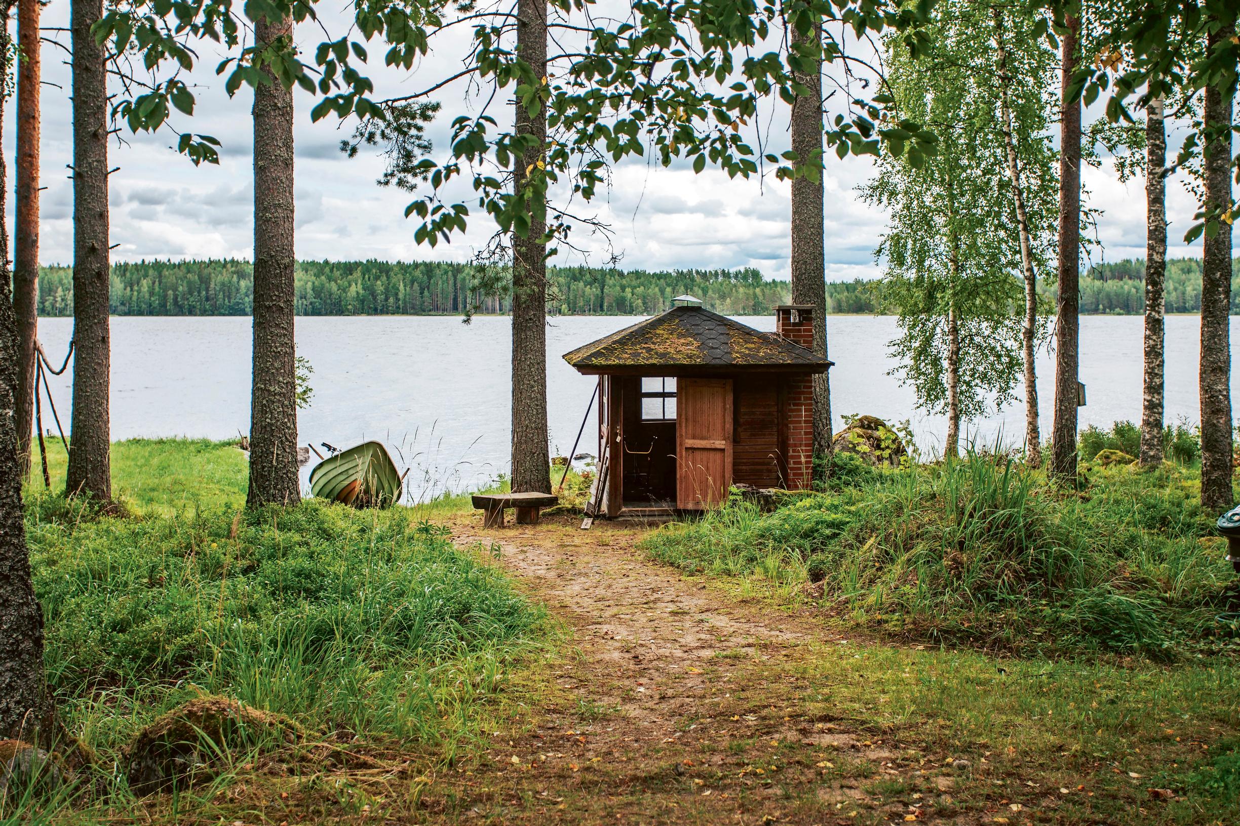 A weathered lakeside shed with a view of the lake through the trees.