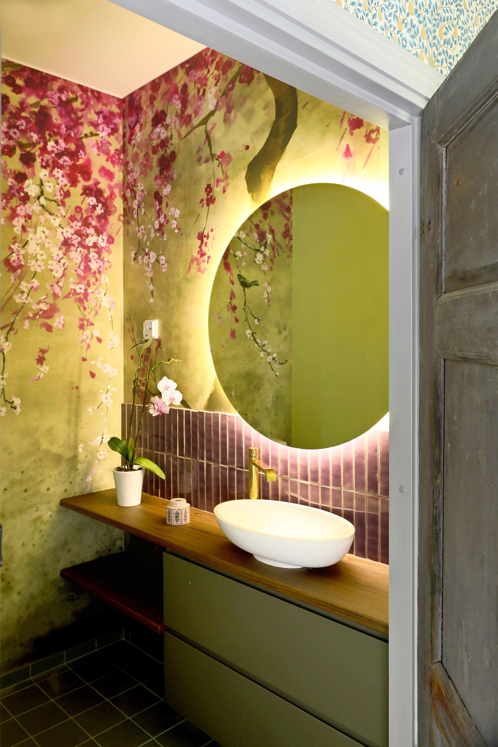 Bathroom with colorful wallpaper. A round mirror hangs above a small hand-washing basin.