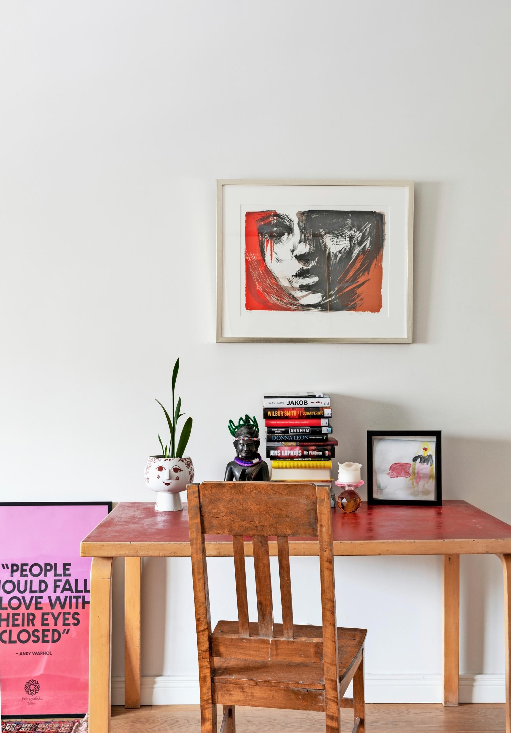 A workspace with a table and chair. There’s a painting on the wall.