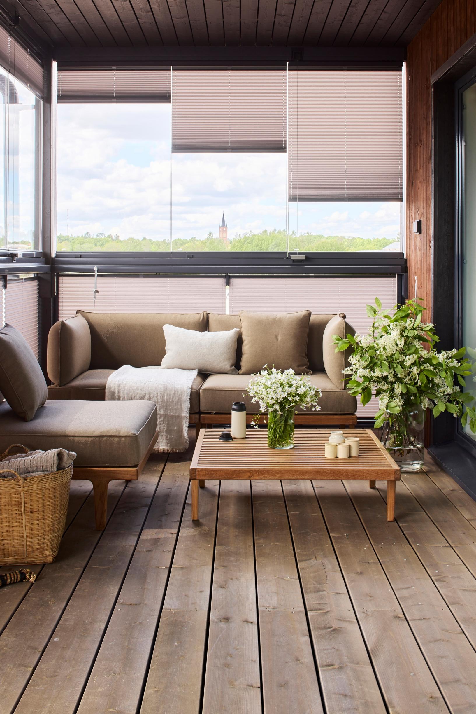 A glazed terrace furnished with lounge-style pieces and protected by balcony blinds