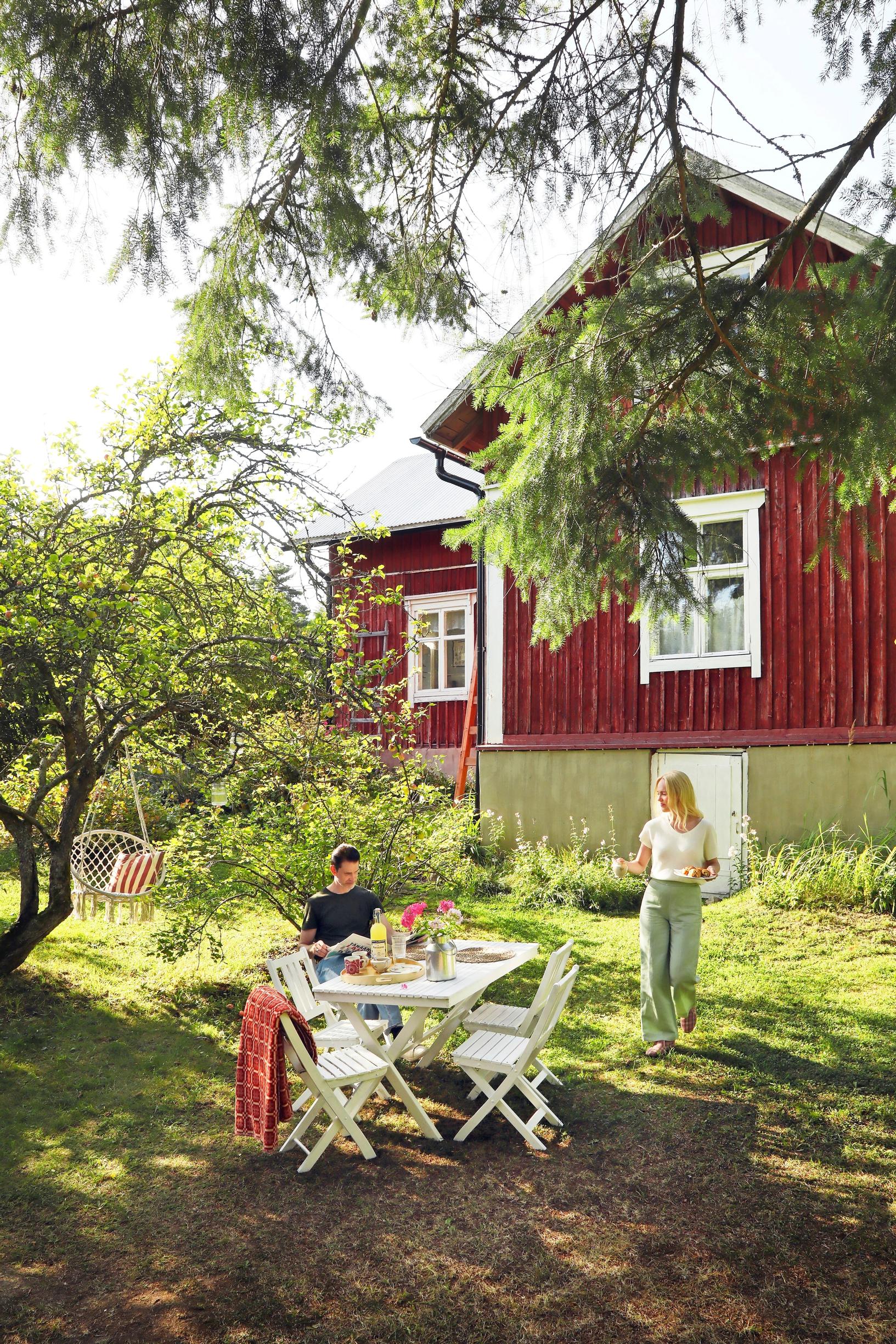 Sami and Jutta Helenius by the garden seating in front of the red log house