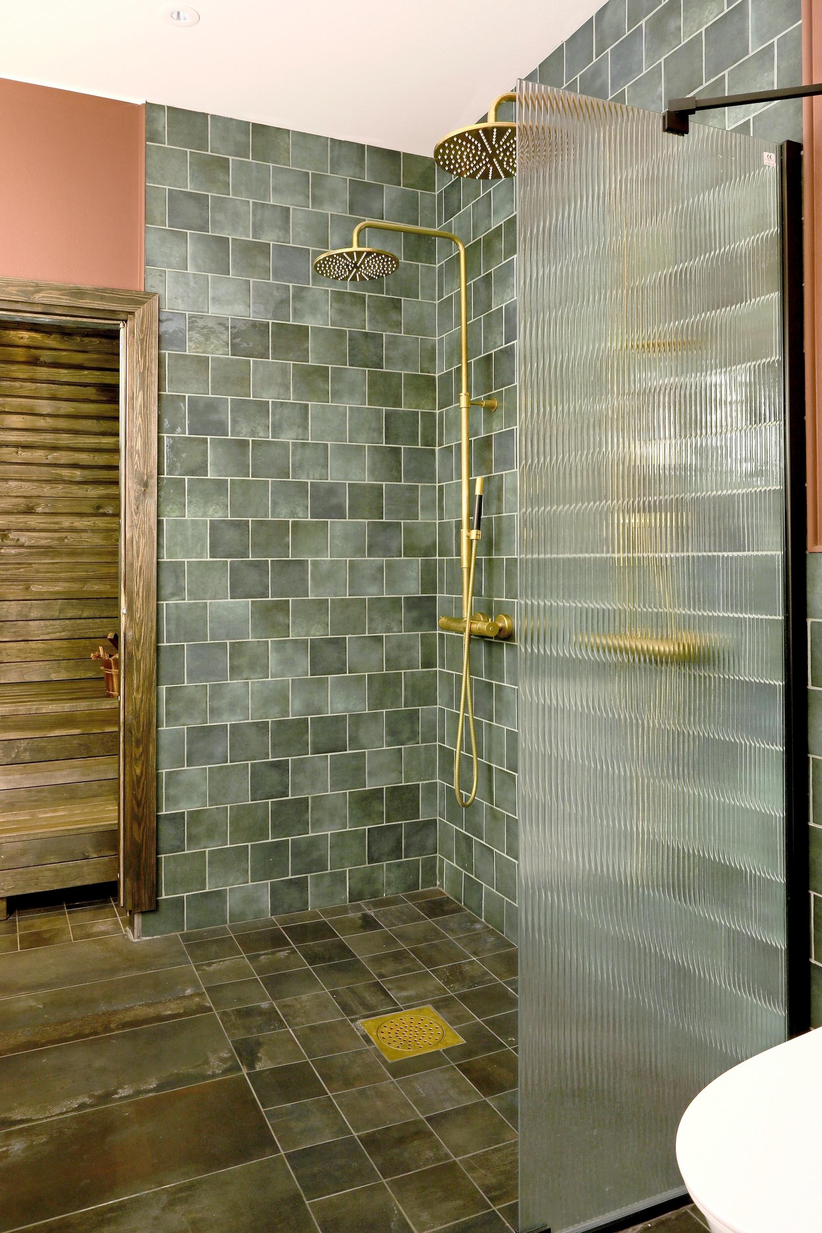 Bathroom with green tiles and two brass-colored showers.