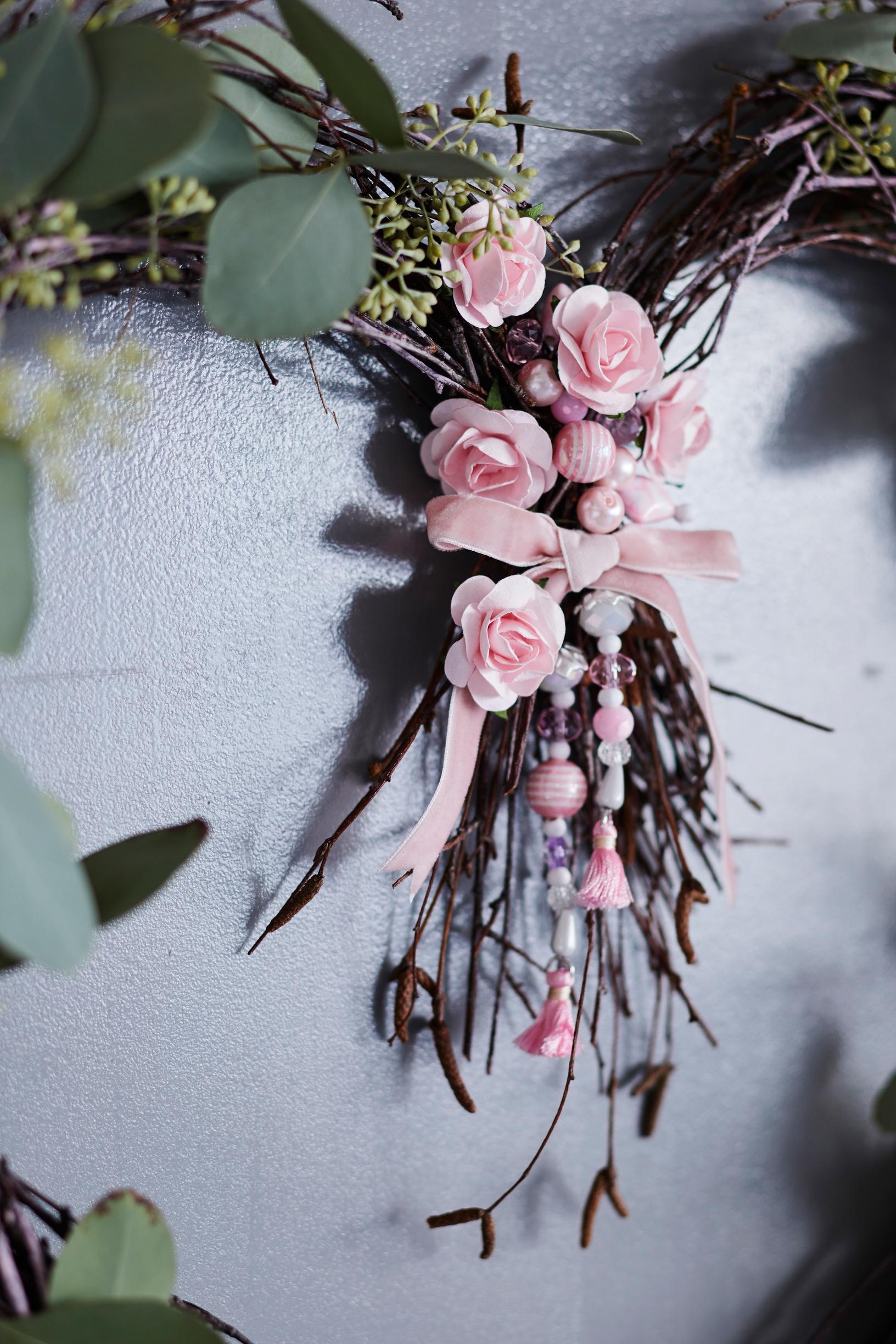 Heart-shaped twig wreath decorated with beads, a bow and flowers