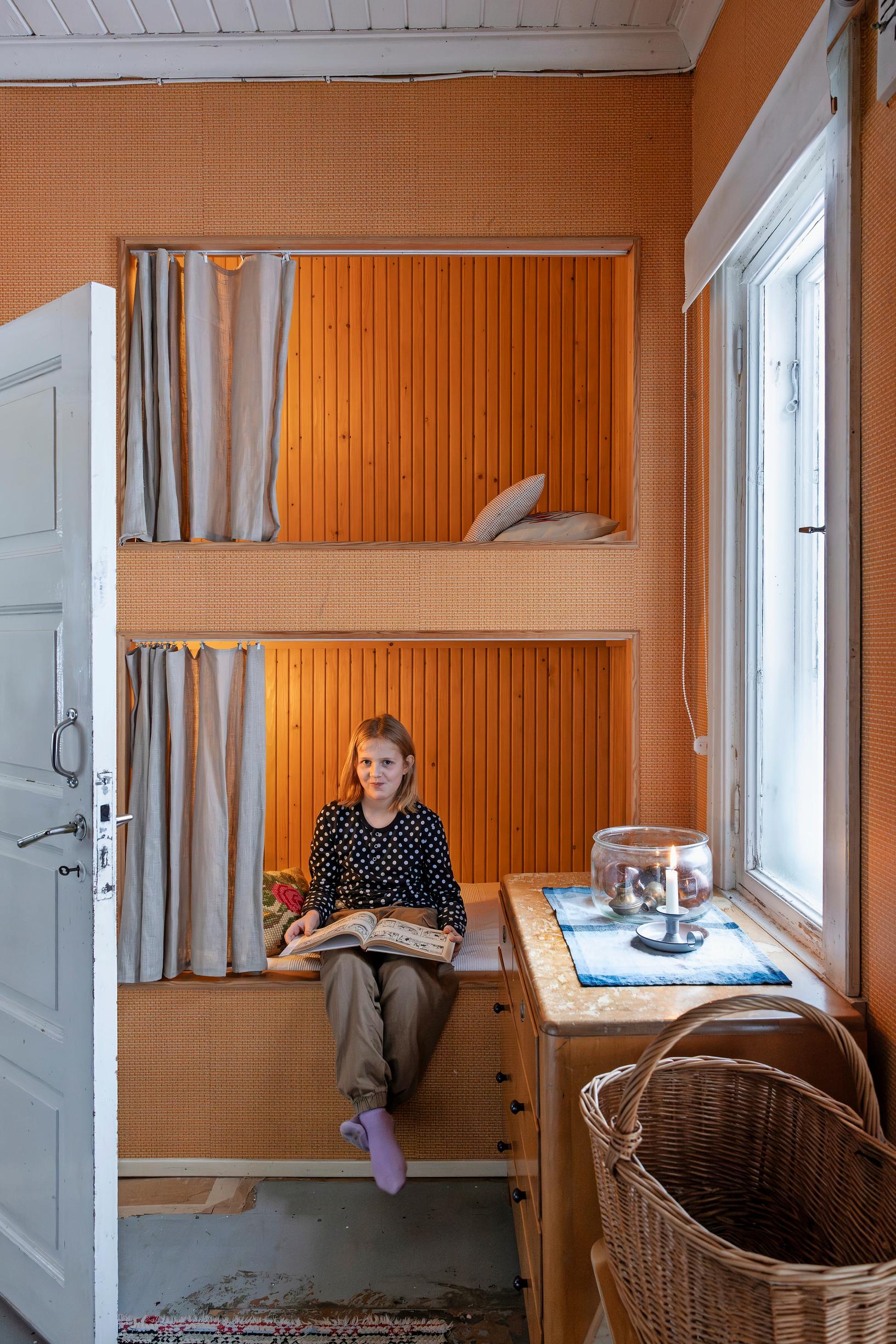 A girl sitting on the lower bunk of a traditional bunk bed reading a book.