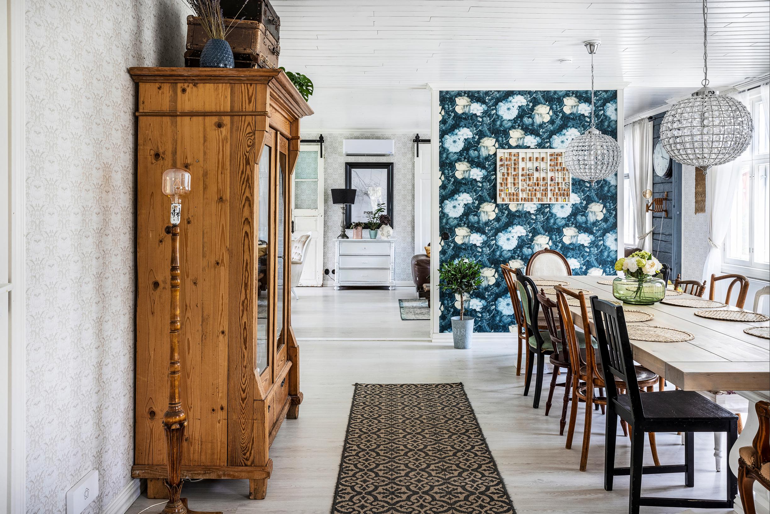 A dining area with a large table and cabinet, plus blue floral wallpaper
