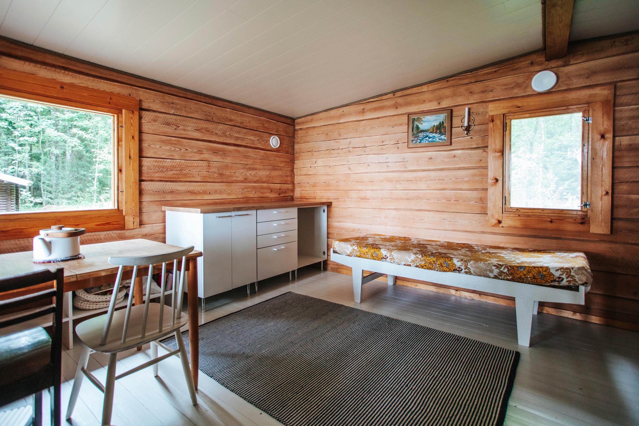 The log cottage’s living room, a dresser, a spindle-back chair, a table, and a bed.